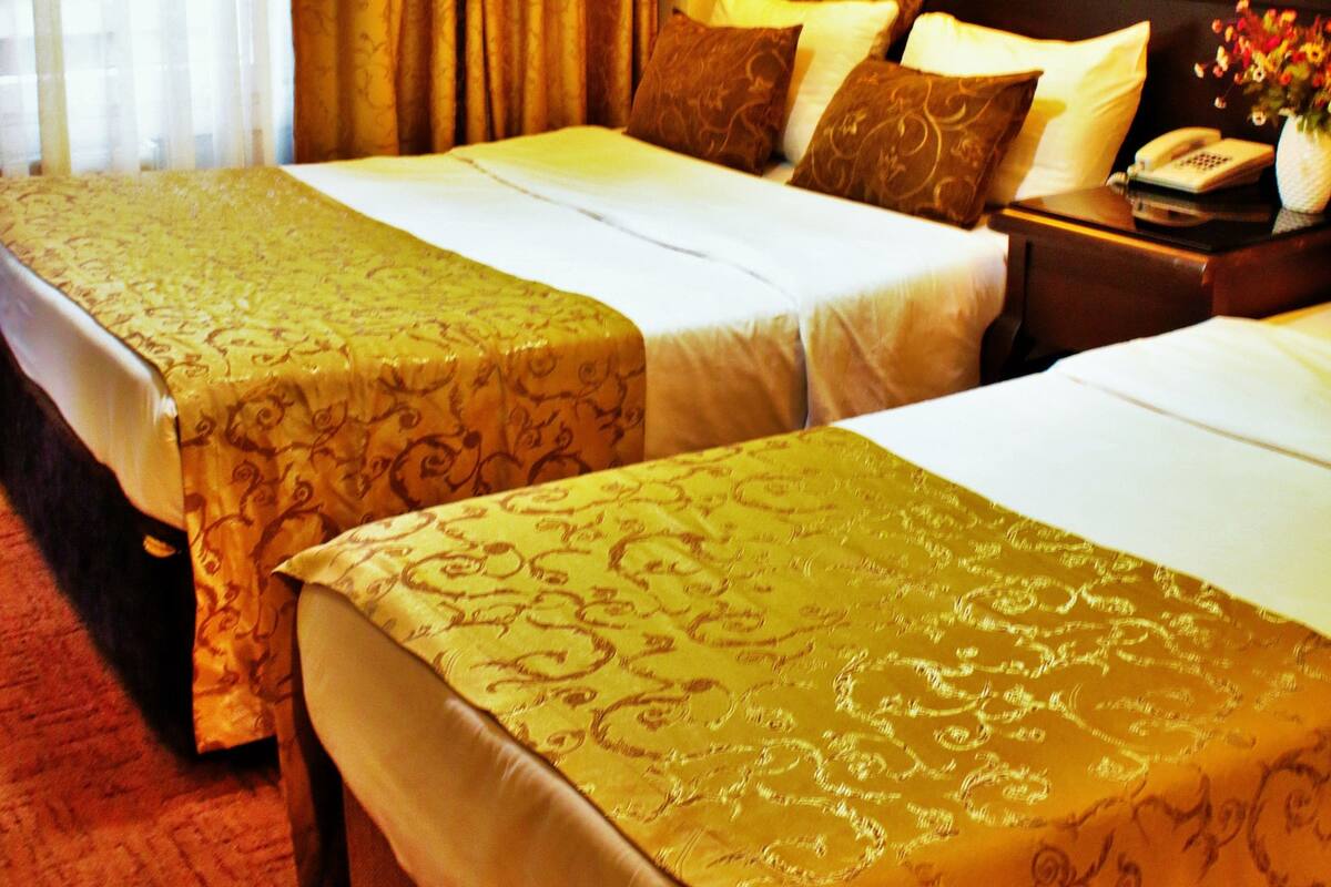 A hotel room with two beds, a nightstand with a phone and vase, and a large window with curtains.