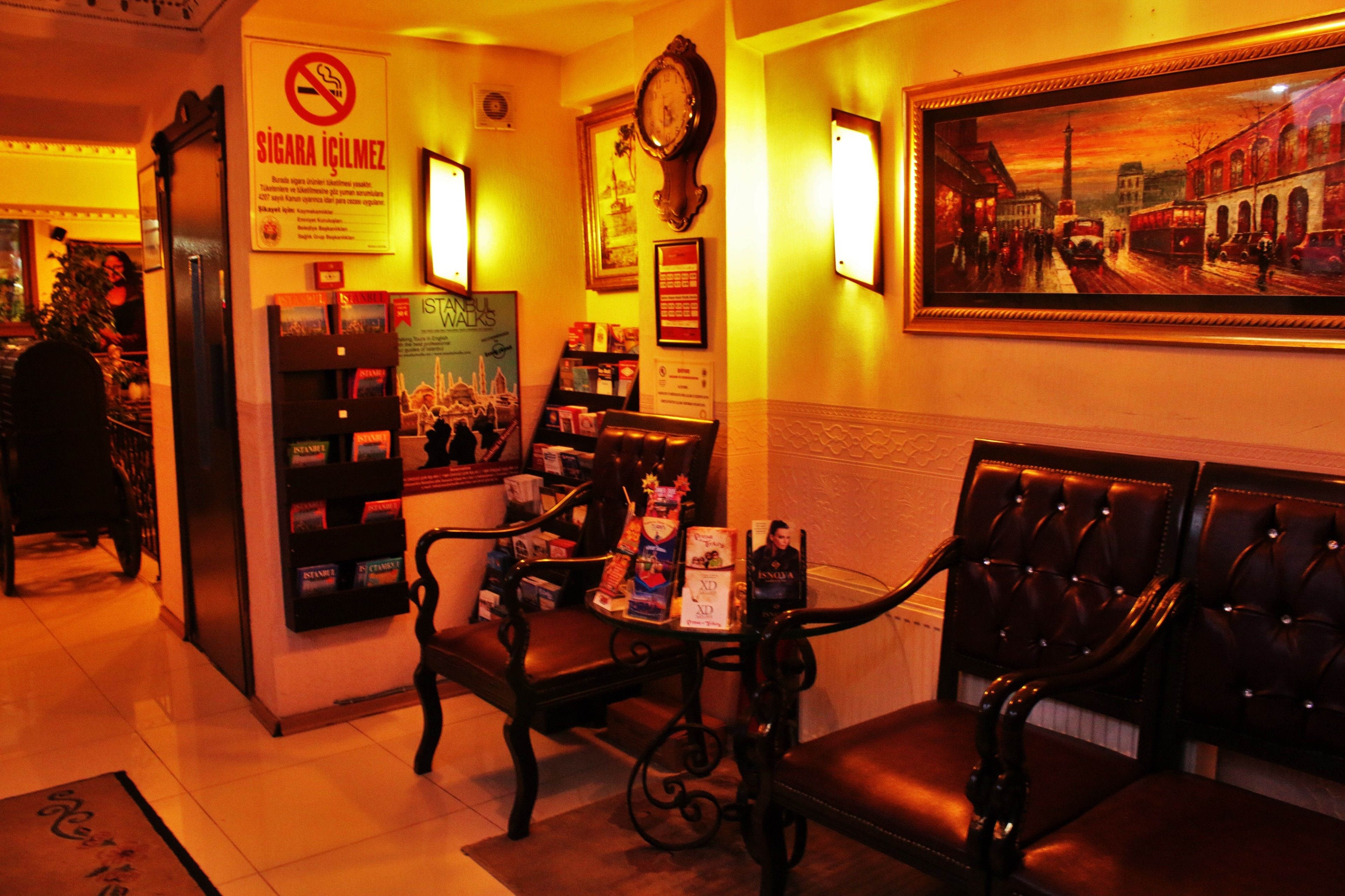 A lobby with leather seating, a clock, framed artwork, and a sign with a no-smoking symbol.