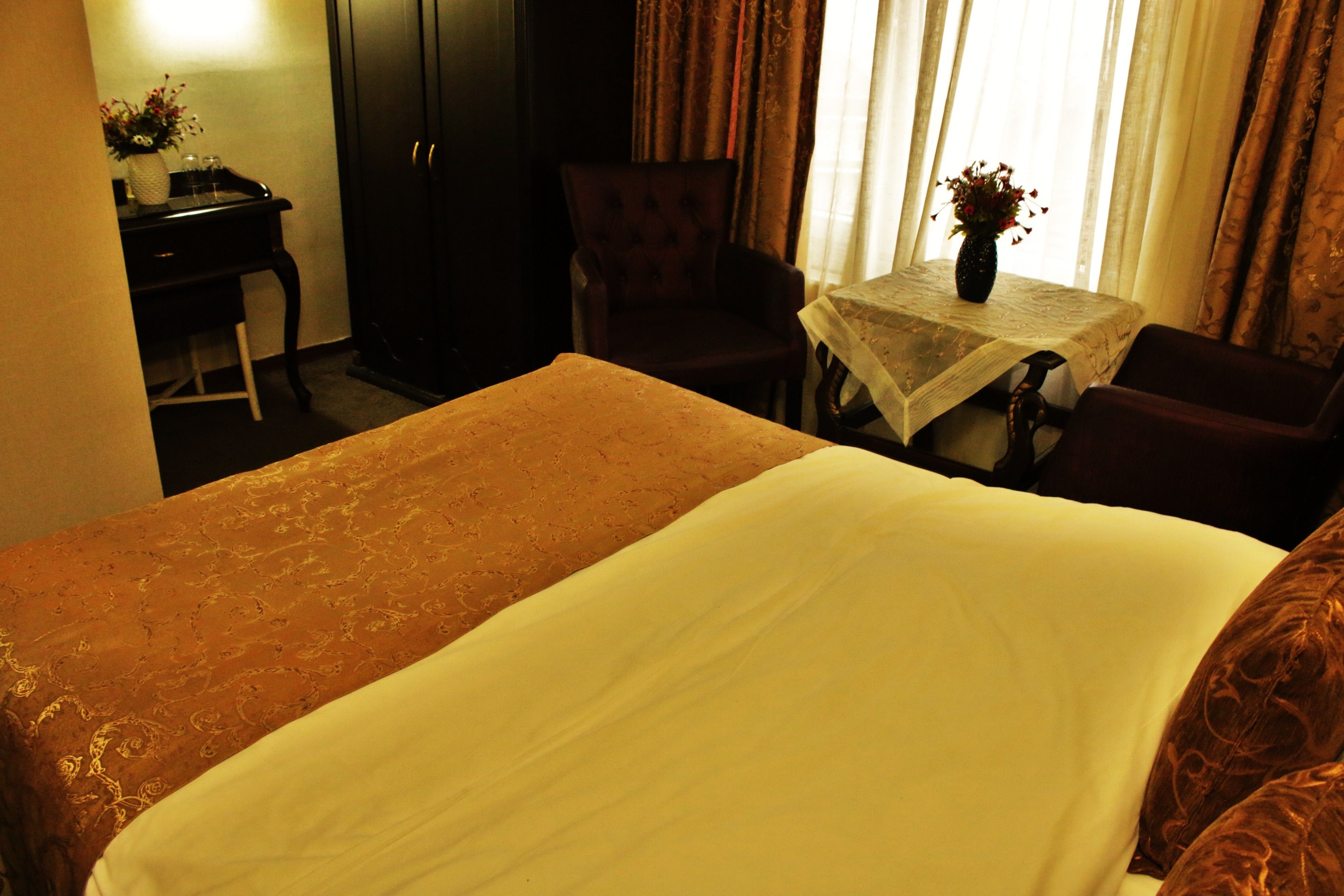 A hotel room with a large bed, a desk with a vase of flowers, a chair, and a small table with a tablecloth.