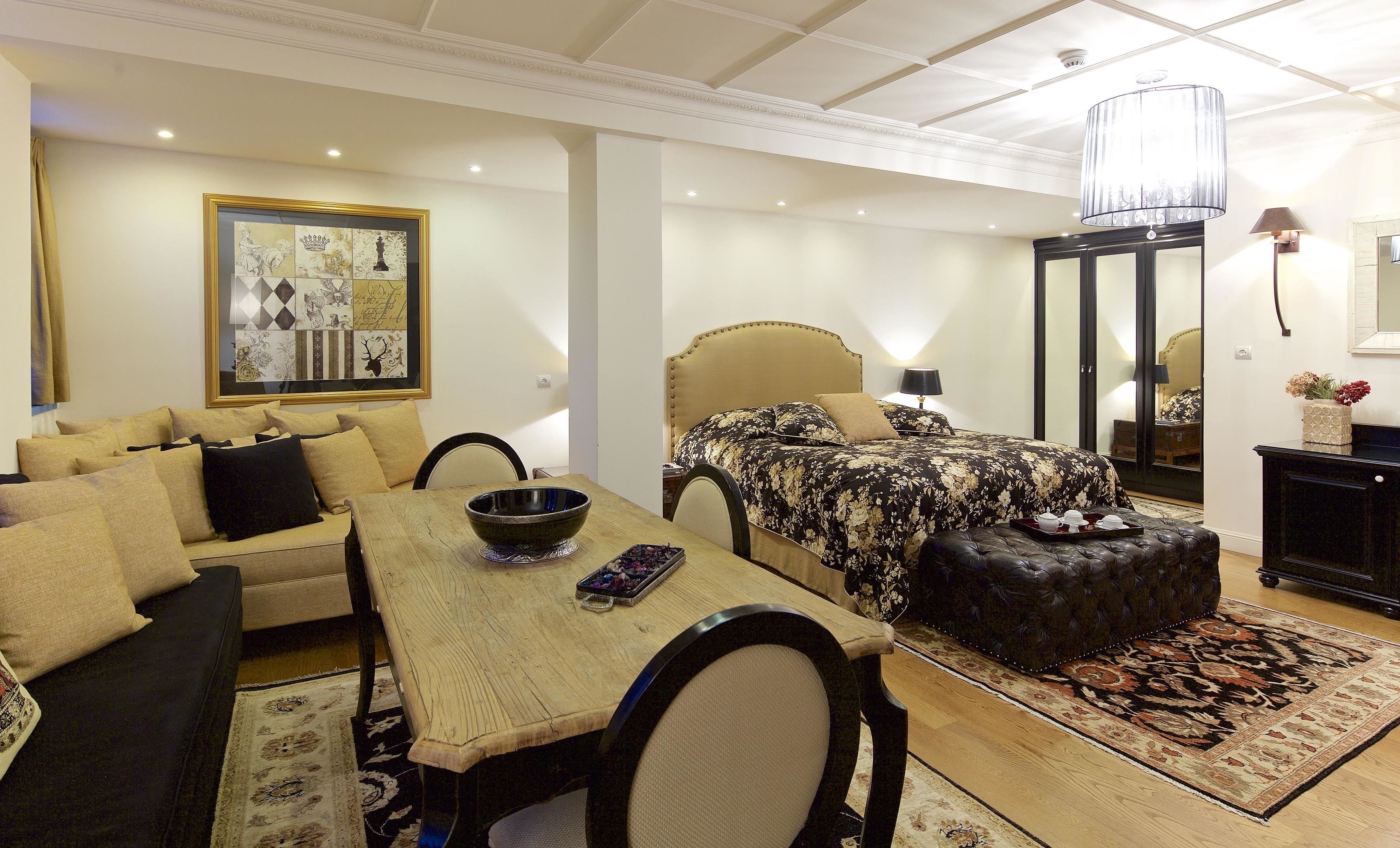 A hotel room with a bed, a sofa, a dining table, and a chandelier.