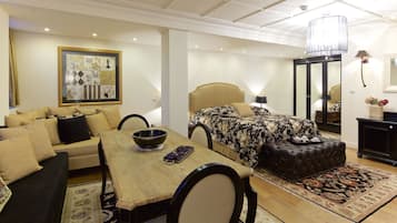 A hotel room with a bed, a sofa, a dining table, and a chandelier.