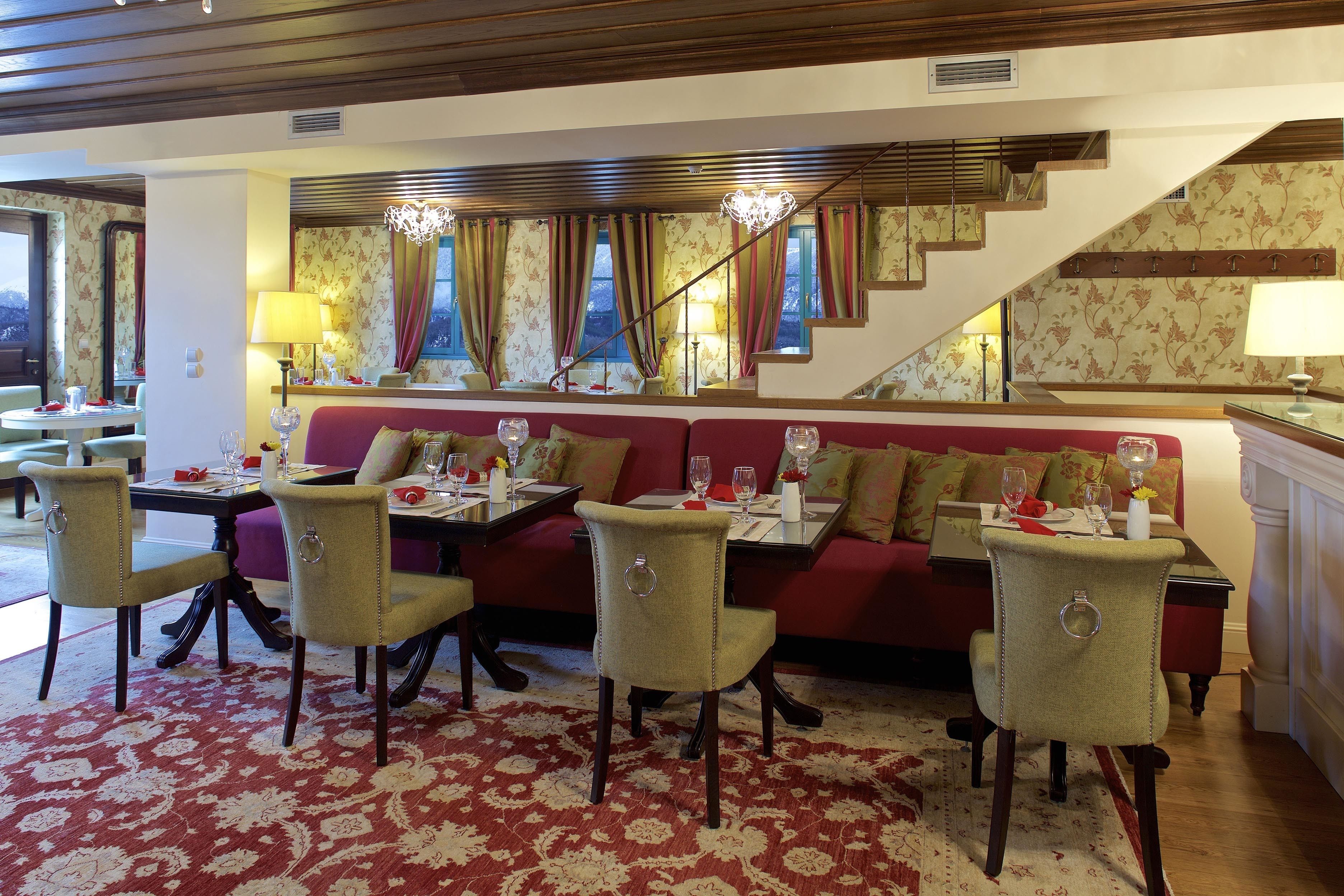 A dining area with a red sofa, four chairs, a table set with wine glasses, and a staircase in the background.