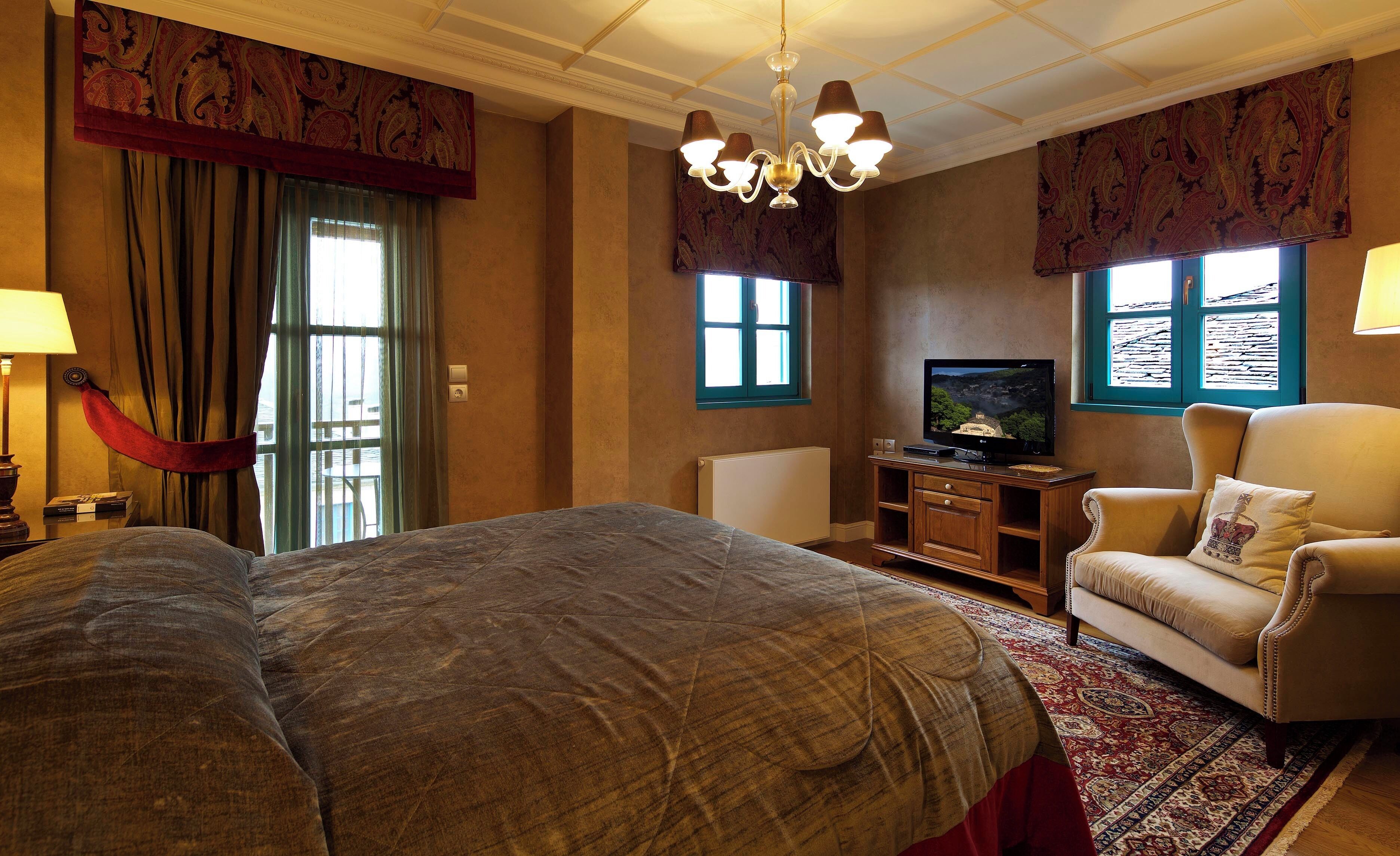 A hotel room with a large bed, a television, a sofa, and a chandelier.