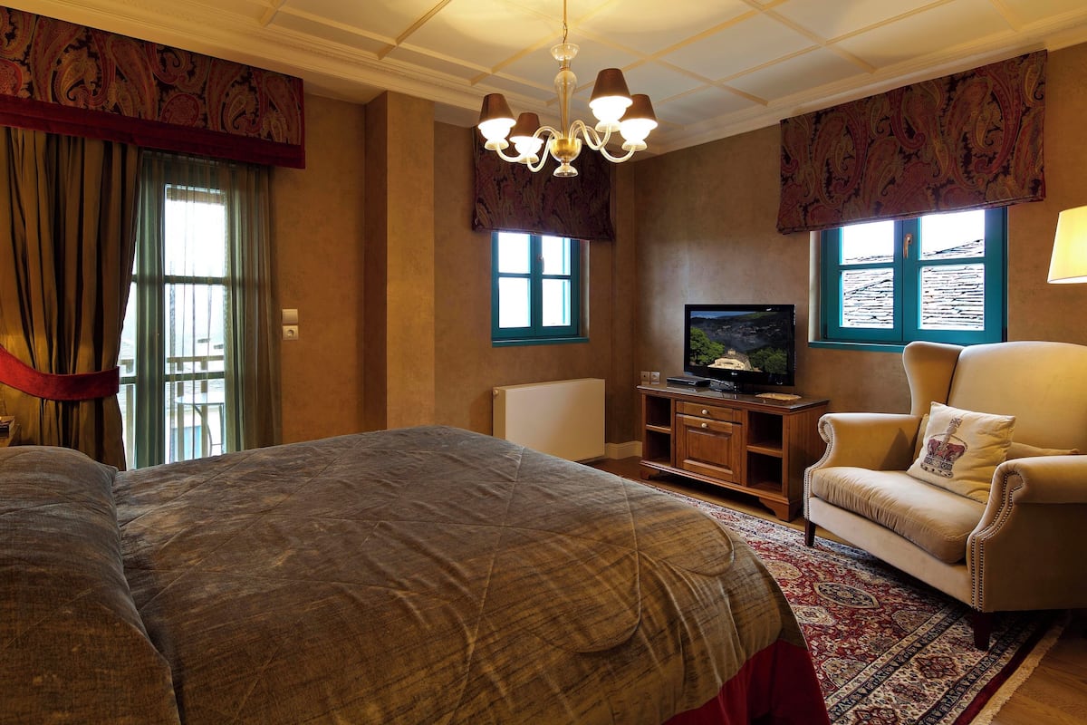 Une chambre d’hôtel avec un grand lit, une télévision, un canapé et un lustre.