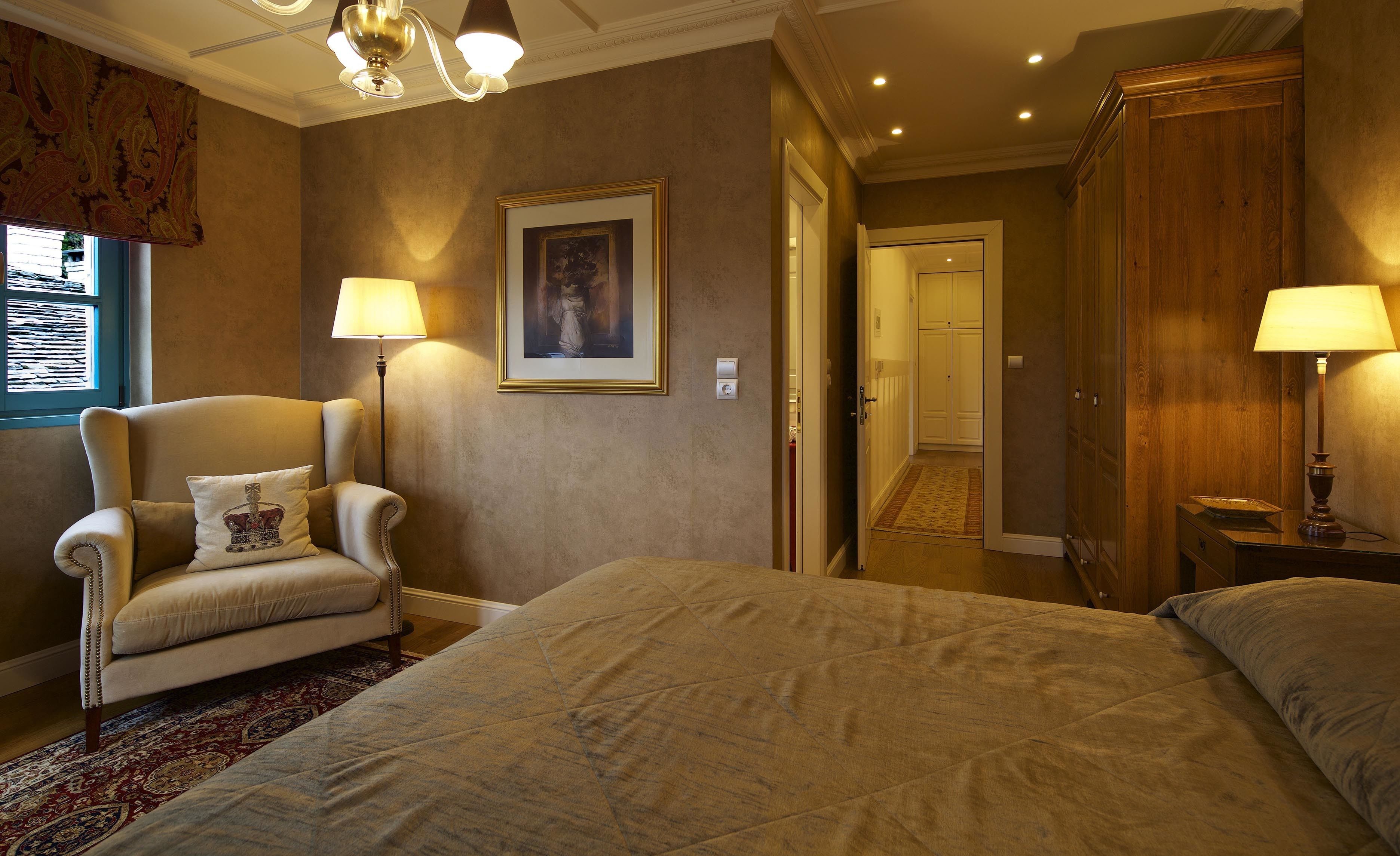 A hotel room with a large bed, a chair, a desk, and a wardrobe. There is a painting on the wall and a window with curtains.