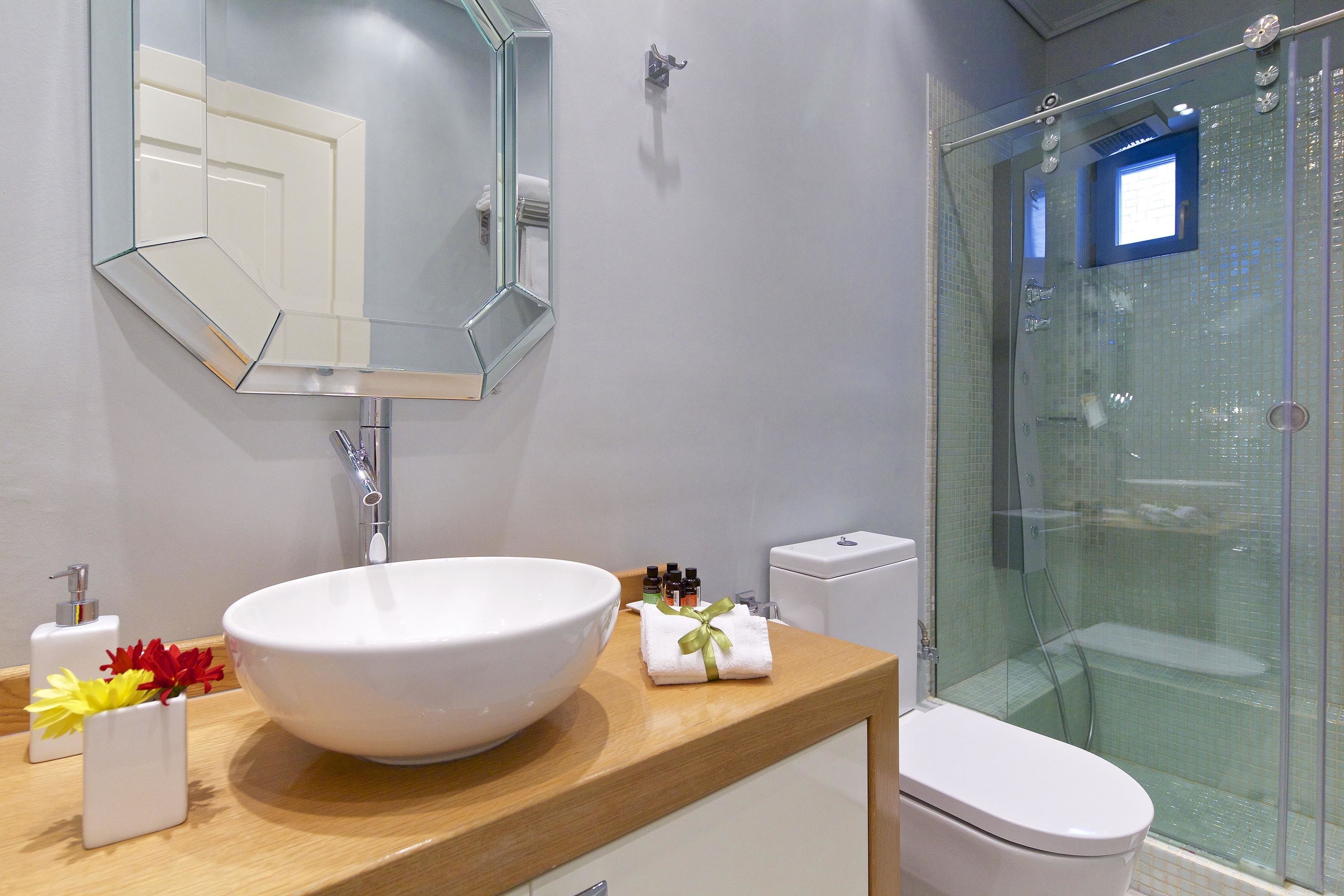 Un baño con un lavamanos grande de color blanco, un espejo, un inodoro y una ducha con mampara de vidrio.