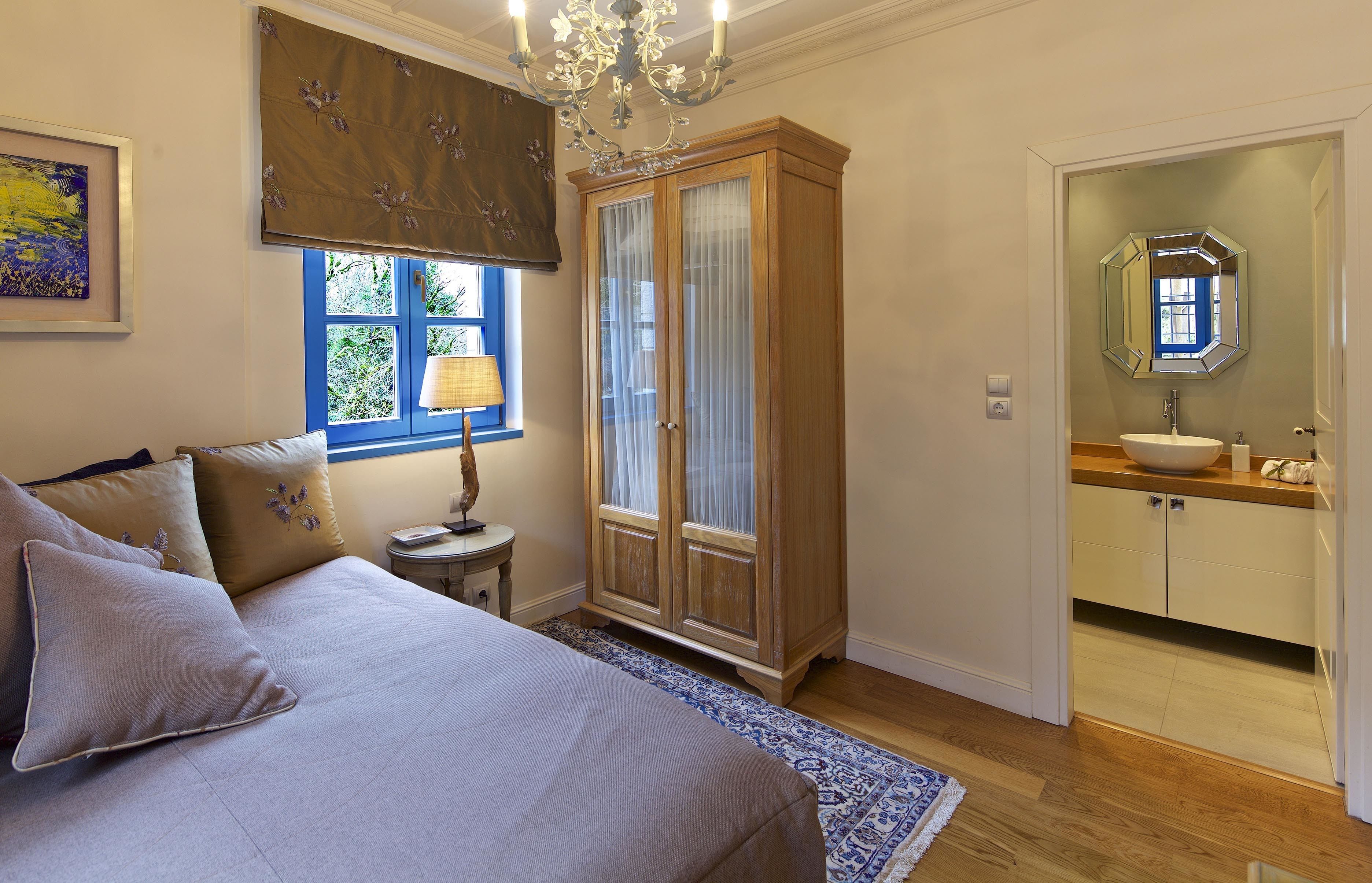 Un dormitorio con cama, mesita de noche, ventana con cortinas, armario y baño con lavabo y espejo.