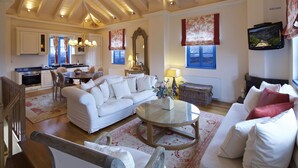 Een ruime woonkamer met een witte bank, een bijzettafeltje en een eettafel. Achtergrond is een keuken met witte kastjes en een raam.