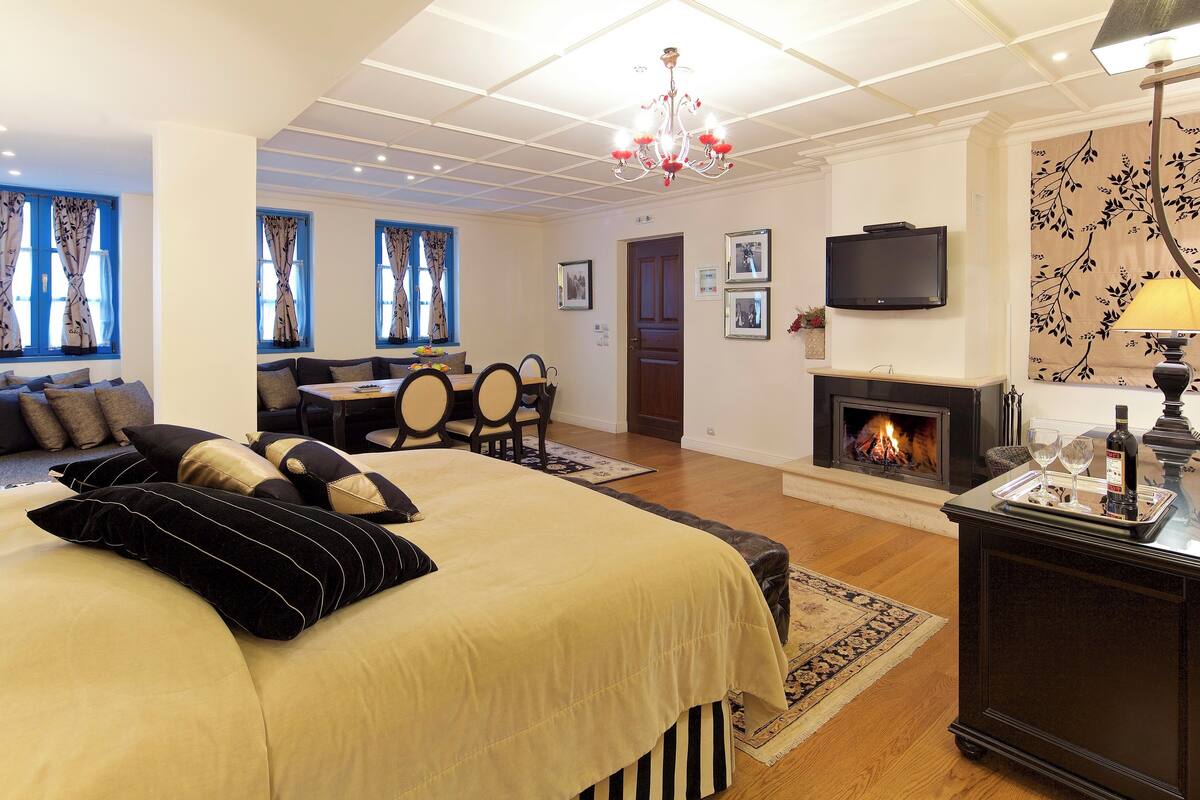 Hotelkamer met een groot bed, een bank, een eettafel, stoelen, een open haard, een televisie en een kroonluchter.