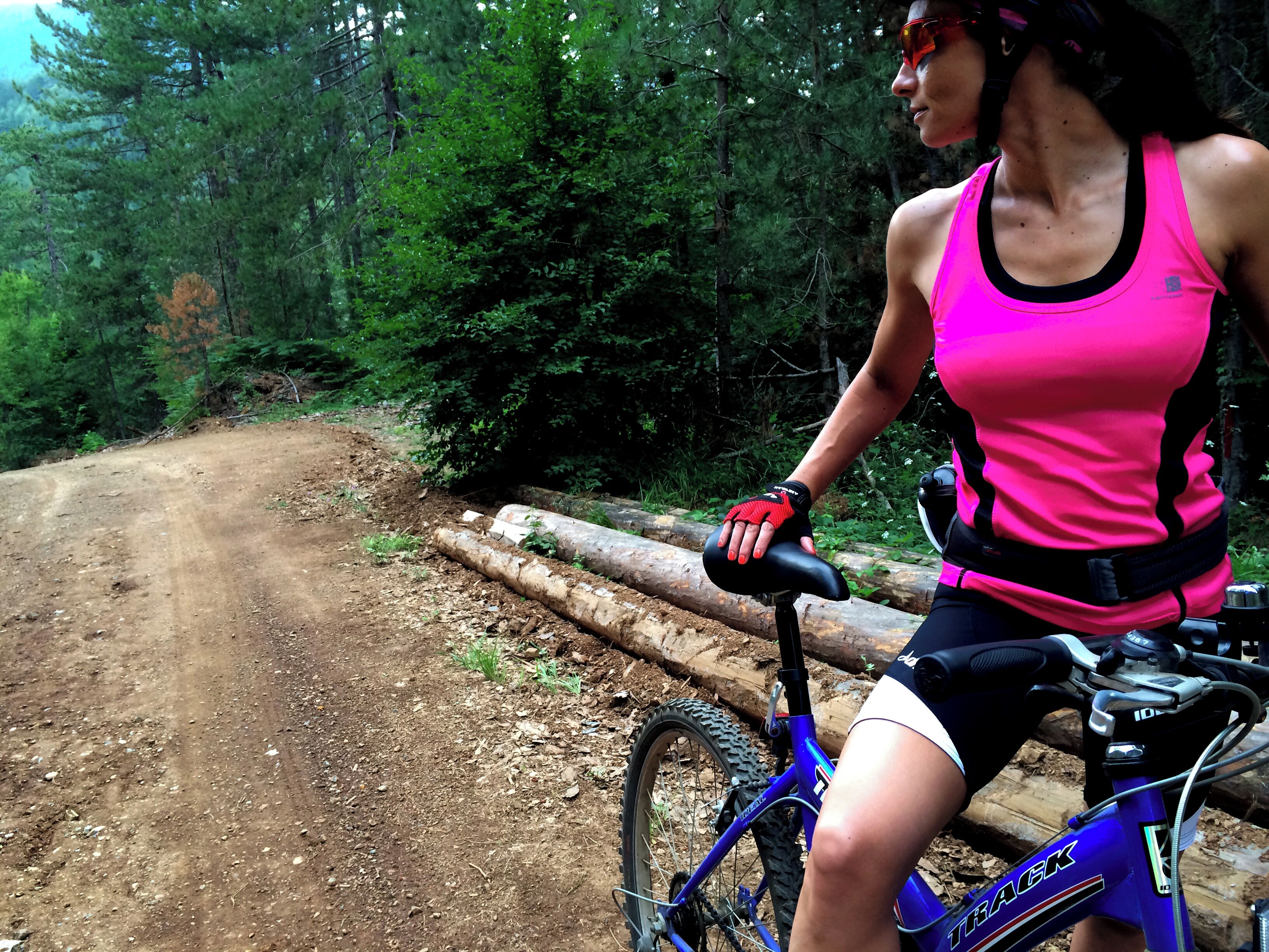 Una persona montando una bicicleta de montaña azul por un sendero de tierra rodeado de un bosque frondoso.