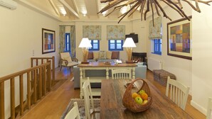Un comedor con una mesa de madera, sillas blancas y una cesta de fruta.