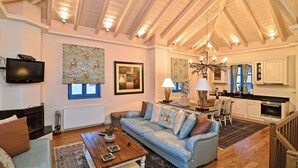 Een ruime woonkamer met een hoge plafond, een open haard, een televisie en een eethoek met een kroonluchter.