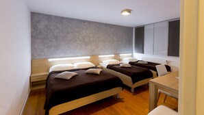 Una habitación de hotel moderna con dos camas, un escritorio de madera y un ventanal grande con persianas.
