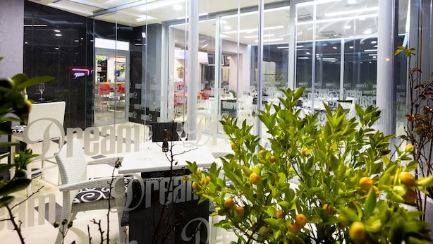 Un comedor interior con paredes de vidrio, muebles blancos y vista al restaurante a través del vidrio.