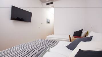 Una habitación de hotel moderna con un televisor de pantalla plana en la pared, una cama bien hecha con ropa blanca, un plaid a rayas y una pequeña mesita de noche con una lámpara y un libro.