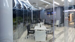 Un restaurante moderno con paredes de vidrio, muebles blancos y vistas a plantas de interior.