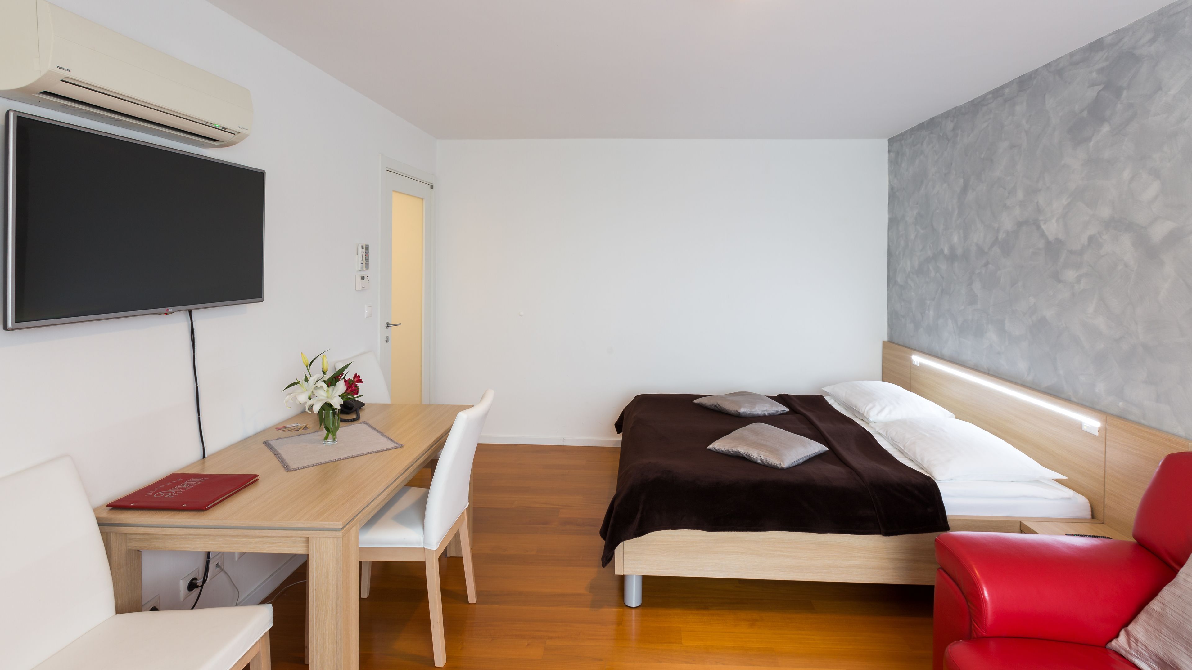 A modern hotel room with a bed, a desk, a chair, and a TV.