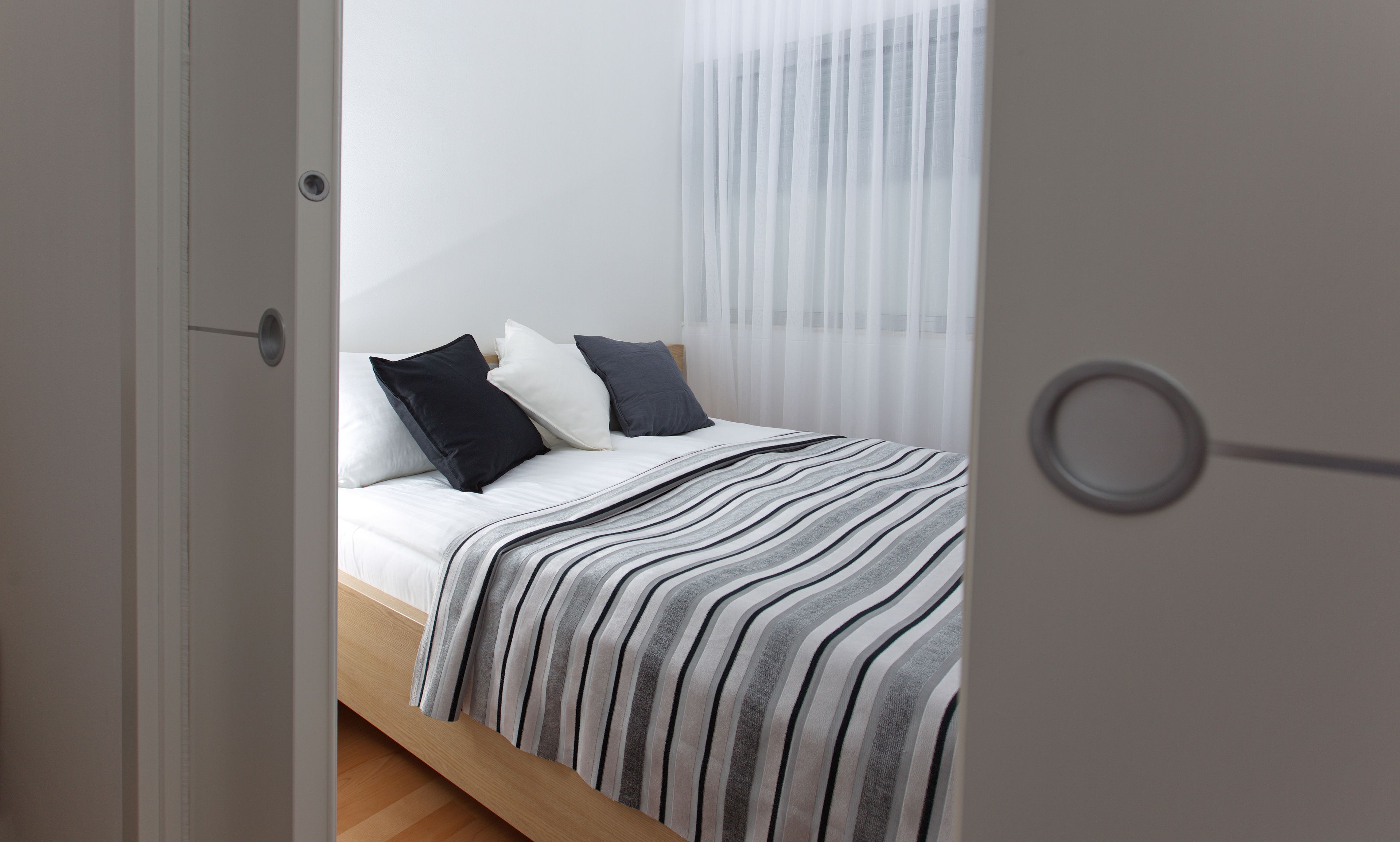 A bedroom with a bed, white curtains, and a striped blanket.