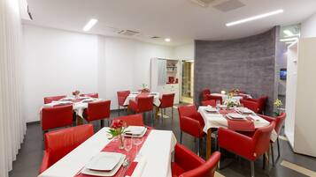 A modern dining area with red chairs and white tables, equipped with flat-screen TVs and a glass partition wall.