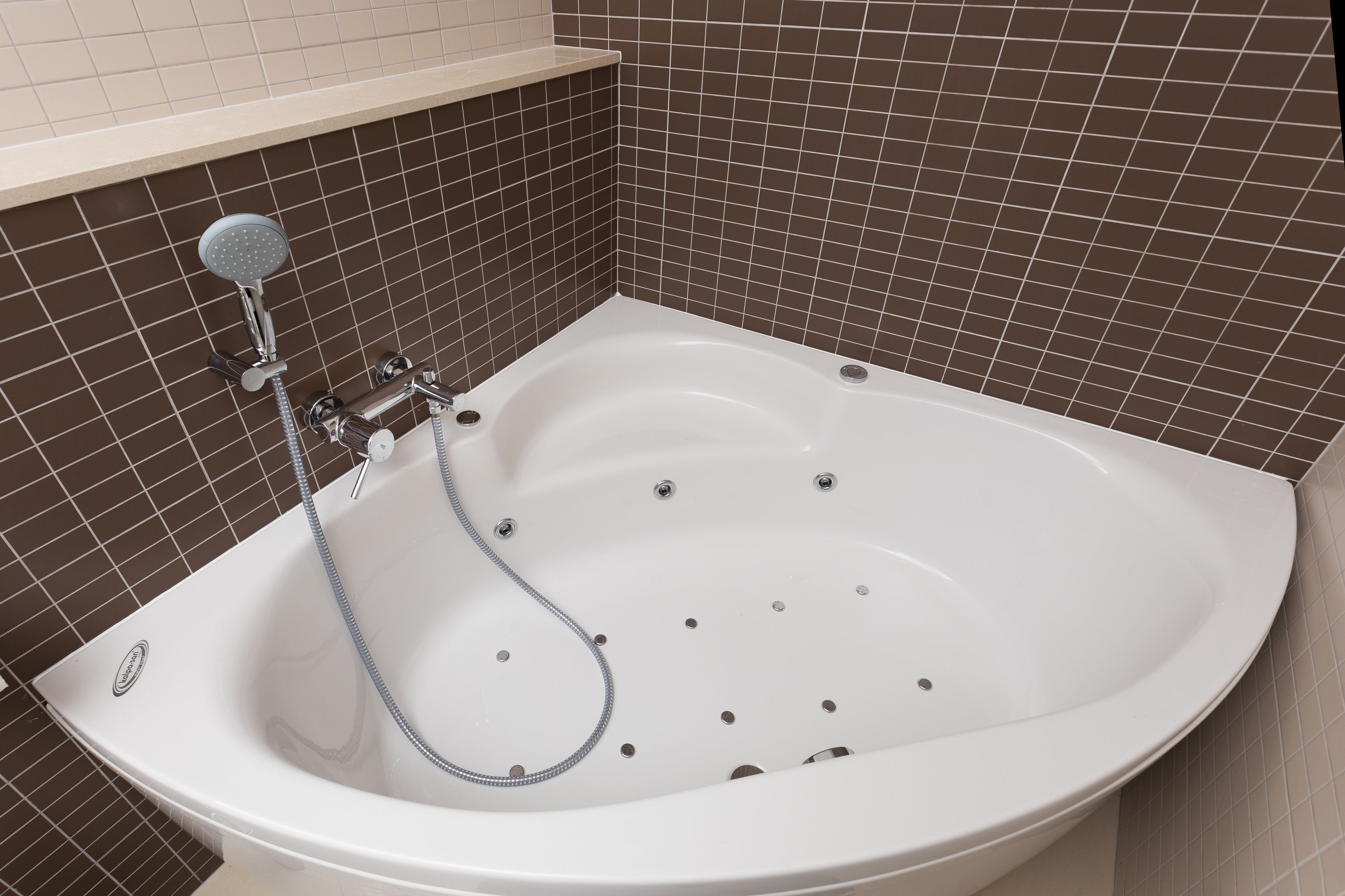 A white bathtub with a handheld showerhead, set against a brown-tiled wall.
