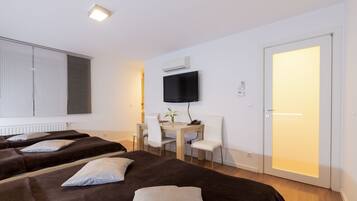Habitación de hotel con dos camas, un escritorio con silla, un televisor y una puerta con luz.