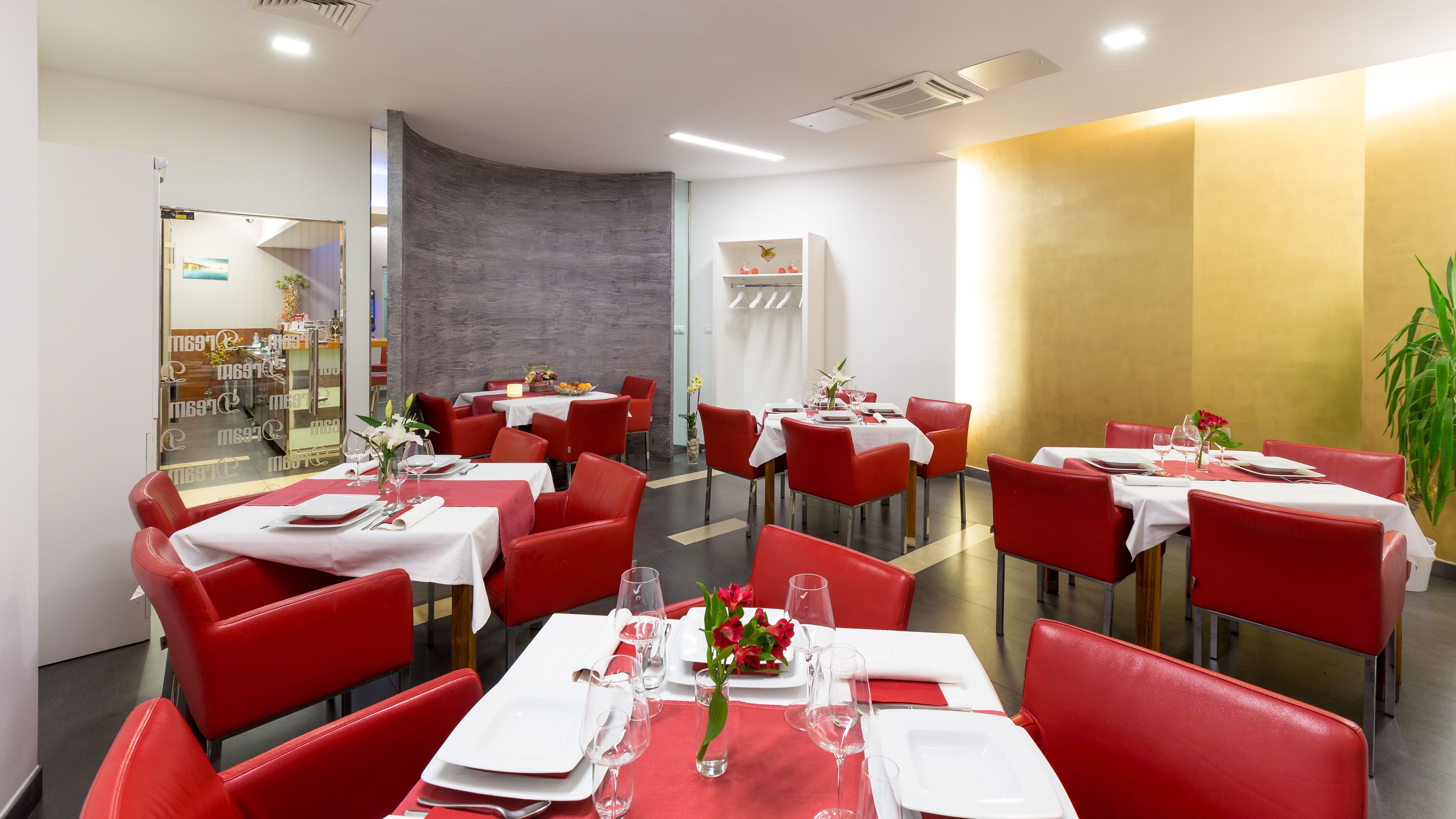 A restaurant with red chairs and white tables, a grey accent wall, and a golden wall.