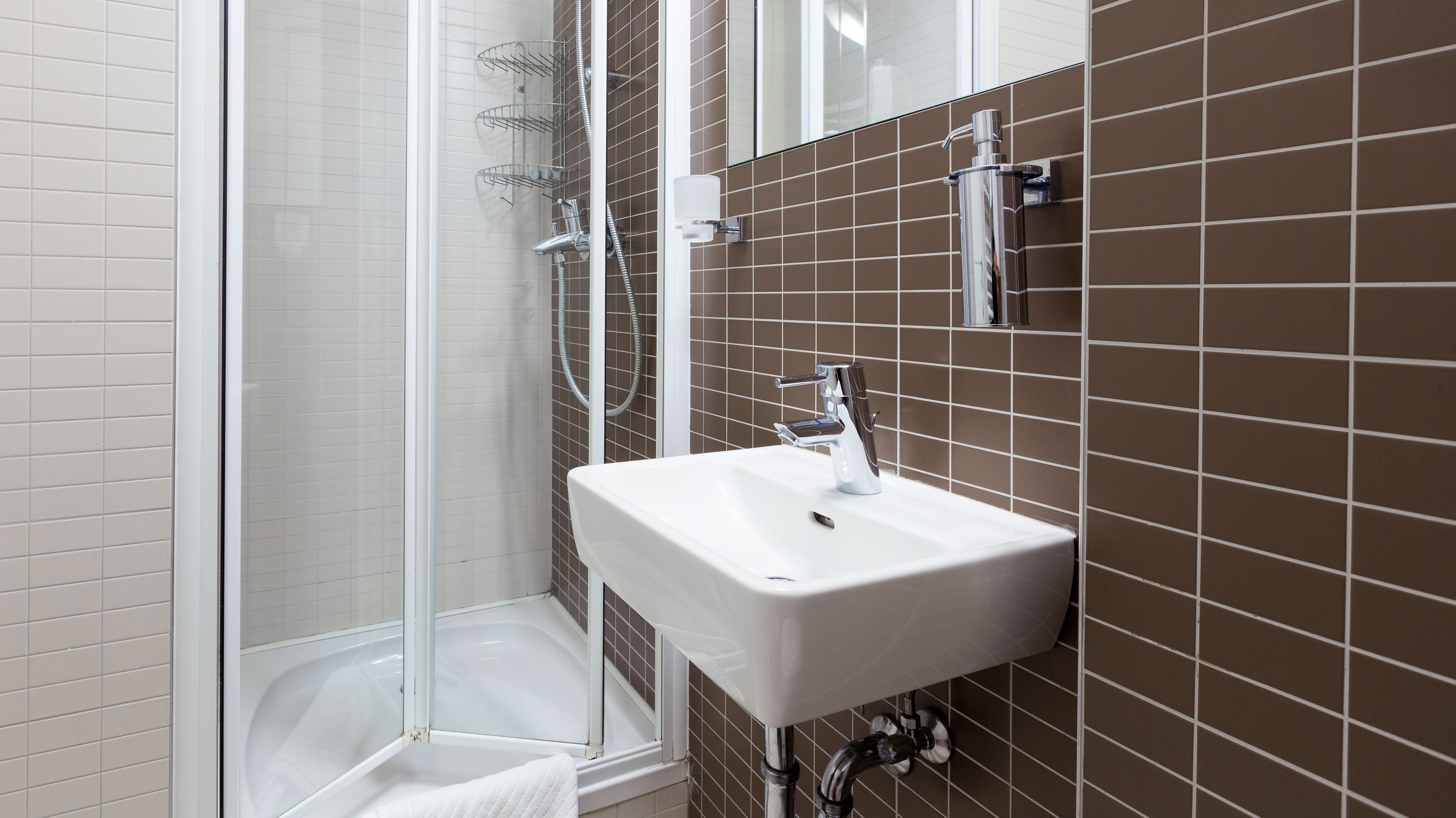 Ein modernes Badezimmer mit einer Duschkabine aus Glas, einem weißen Waschbecken und braunen Fliesenwänden.