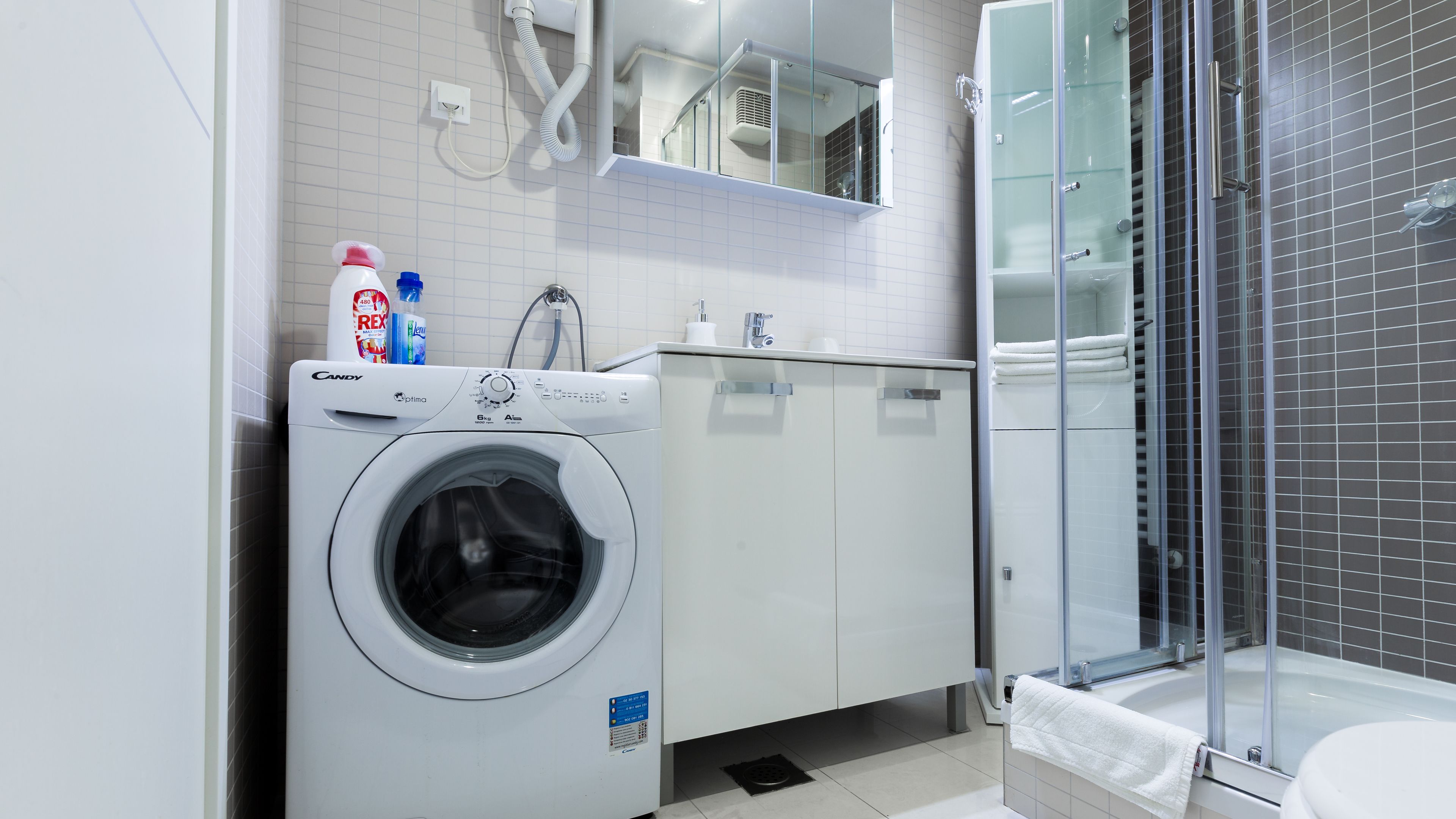 A modern bathroom with a washing machine, a sink, and a glass-enclosed shower.