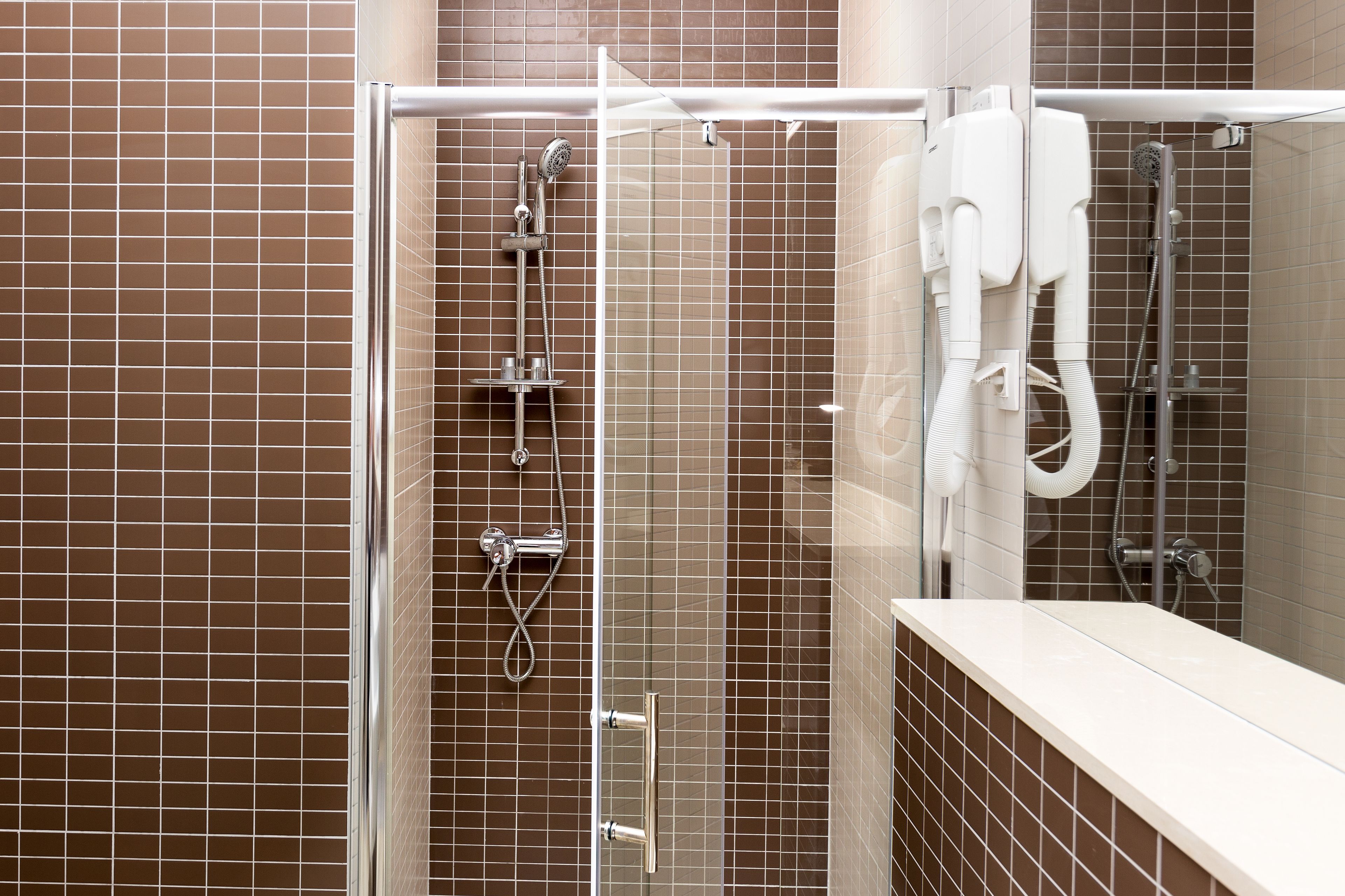 Uma área de chuveiro moderna com divisória de vidro, chuveiro manual e chuveiro fixo na parede, além de um chuveiro manual com mangueira flexível.