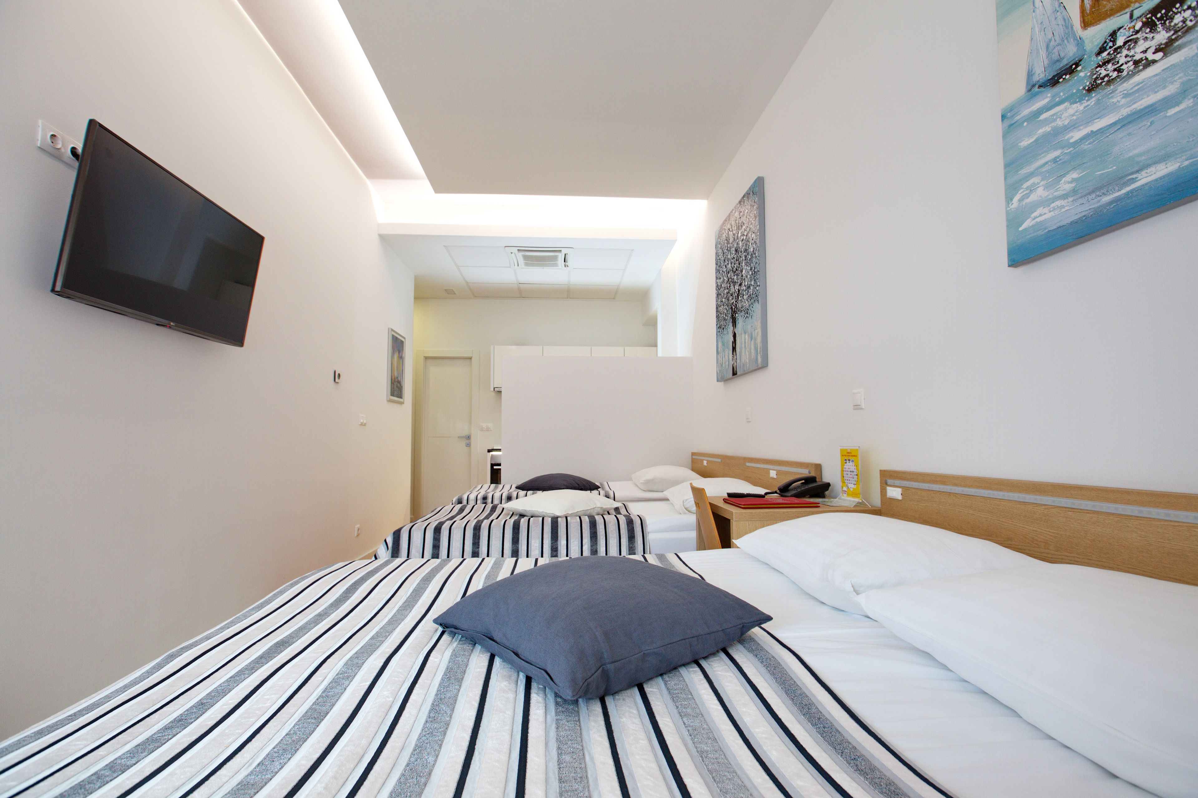 A hotel room with two beds, a TV, a painting, and a view of the hallway.