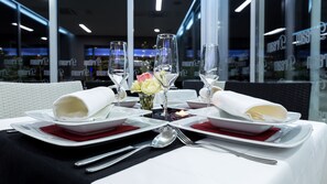 Mesa posta para dois, com pratos brancos, guardanapos dobrados e copos transparentes.