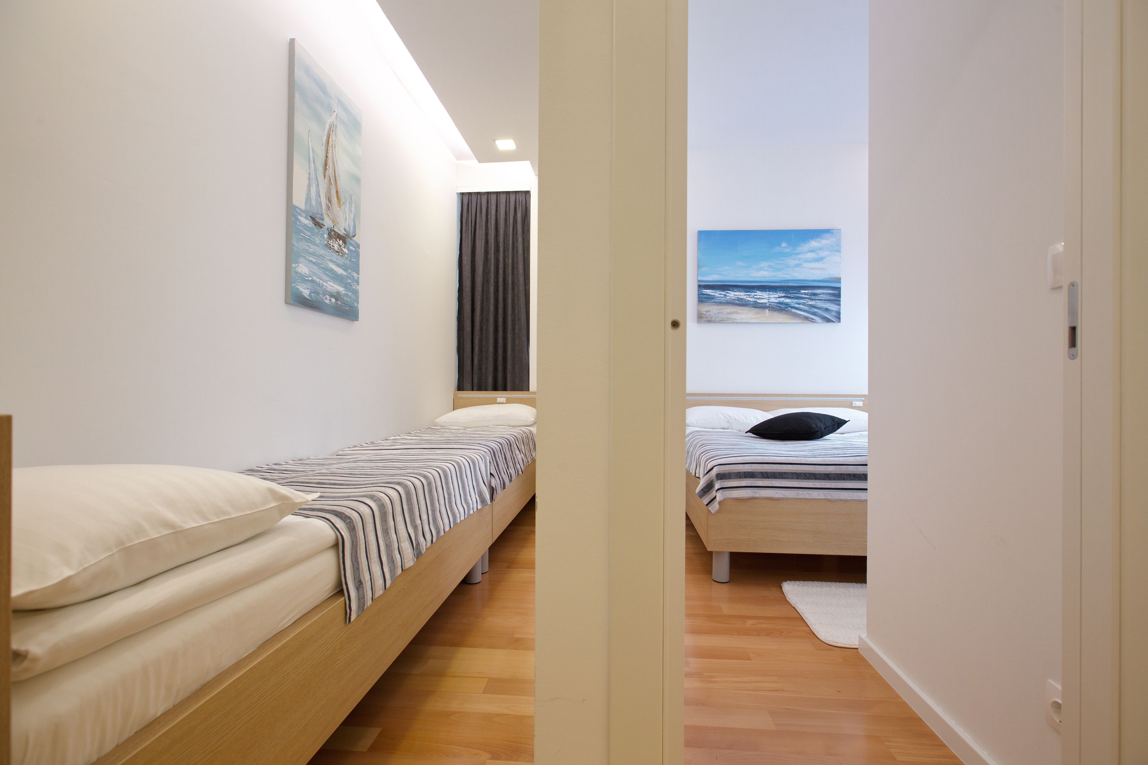 A modern bedroom with two single beds, a large window, and artwork on the walls.
