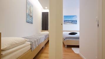 A modern bedroom with two single beds, a large window, and artwork on the walls.