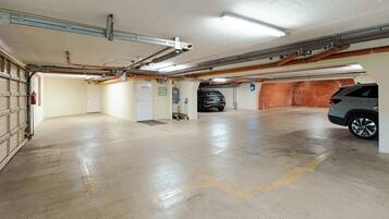 A parking garage with concrete floors, a fire extinguisher, a fire alarm, and a vehicle parked in the distance.