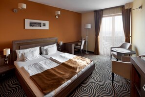 A hotel room with a large bed, a desk, a chair, and a small table.