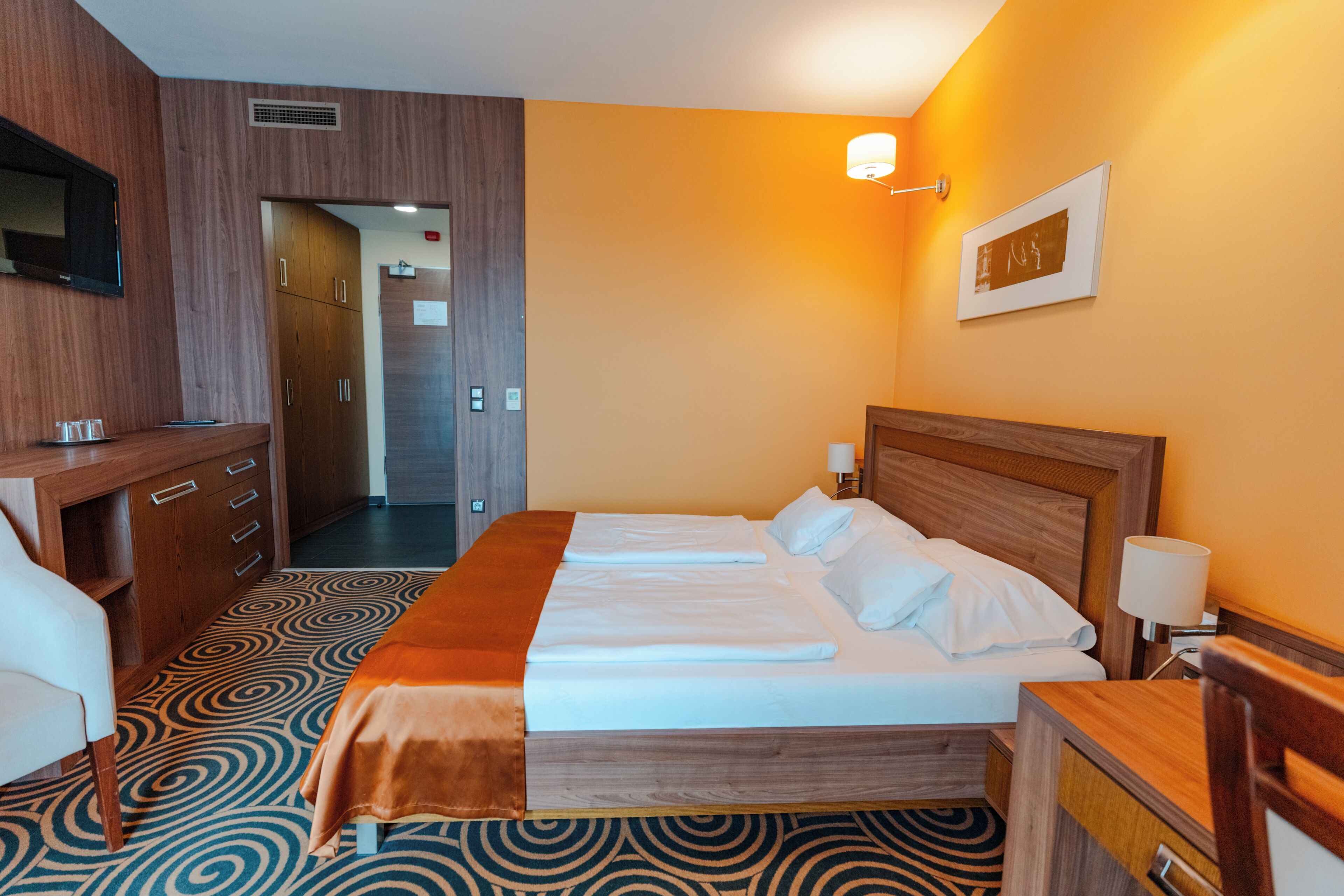 A hotel room with a bed, a desk, a chair, and a television.