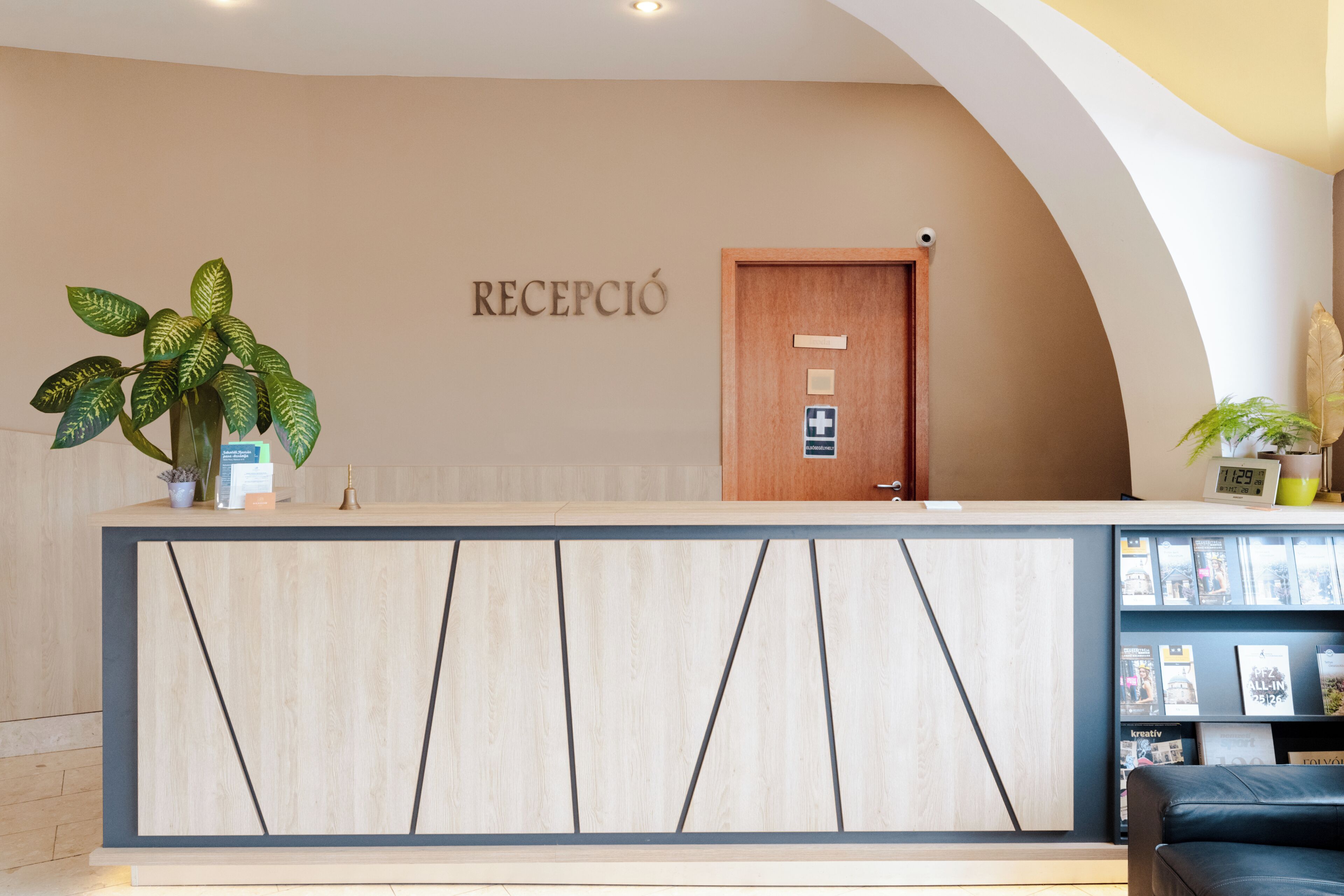 En receptionsdisk med træfinish, en potteplante og et ophængt skilt med teksten 'RECEPCIÓ'.
