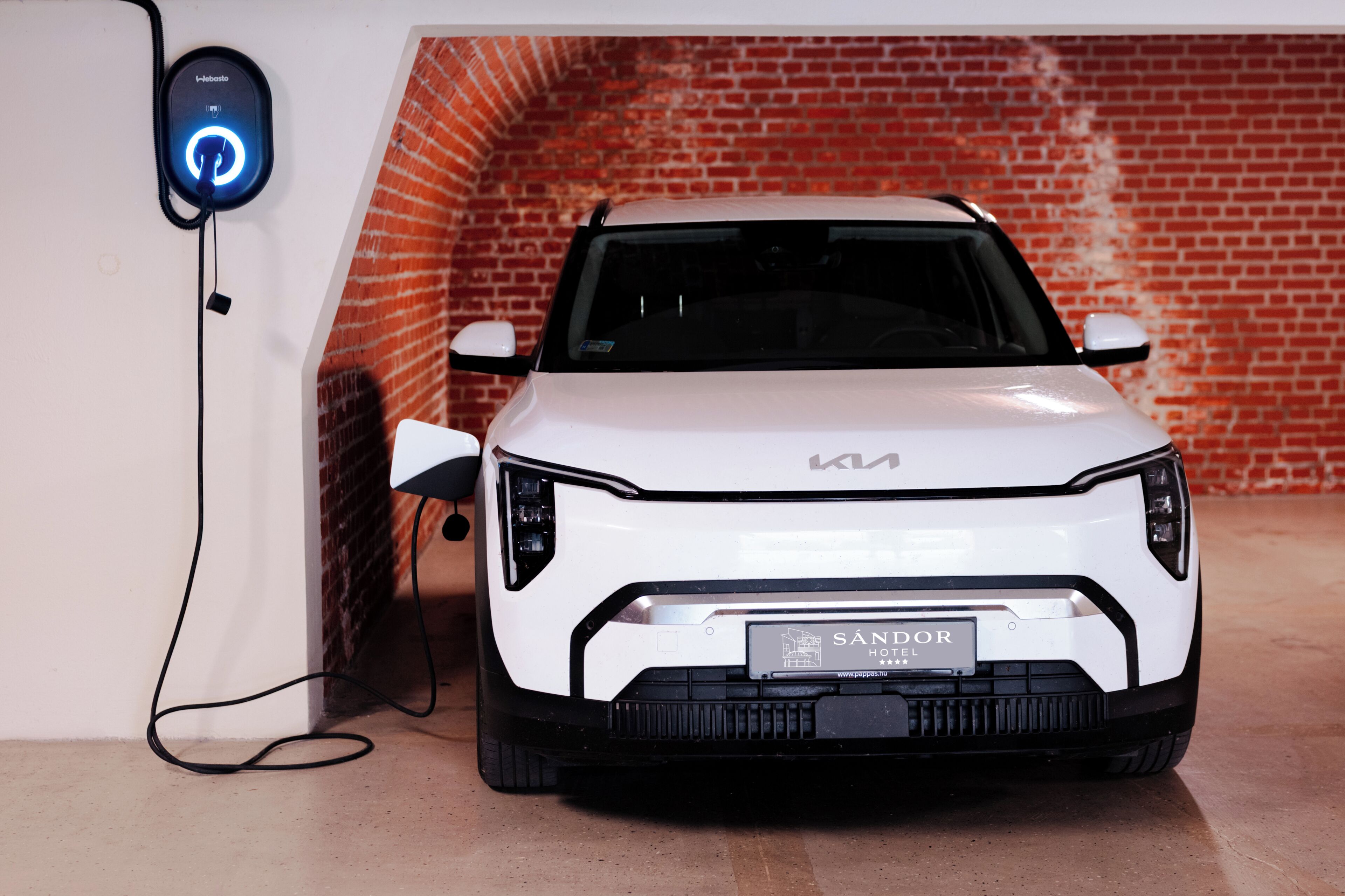 A white Kia car parked in a garage with a brick wall in the background.