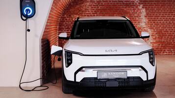 A white Kia car parked in a garage with a brick wall in the background.