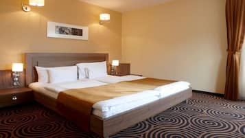 A hotel room with a large bed, two bedside tables with lamps, a headboard, a patterned carpet, and a framed picture on the wall.