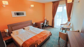 Une chambre d’hôtel avec un grand lit, un bureau, une chaise, une petite table et une fenêtre avec des rideaux.
