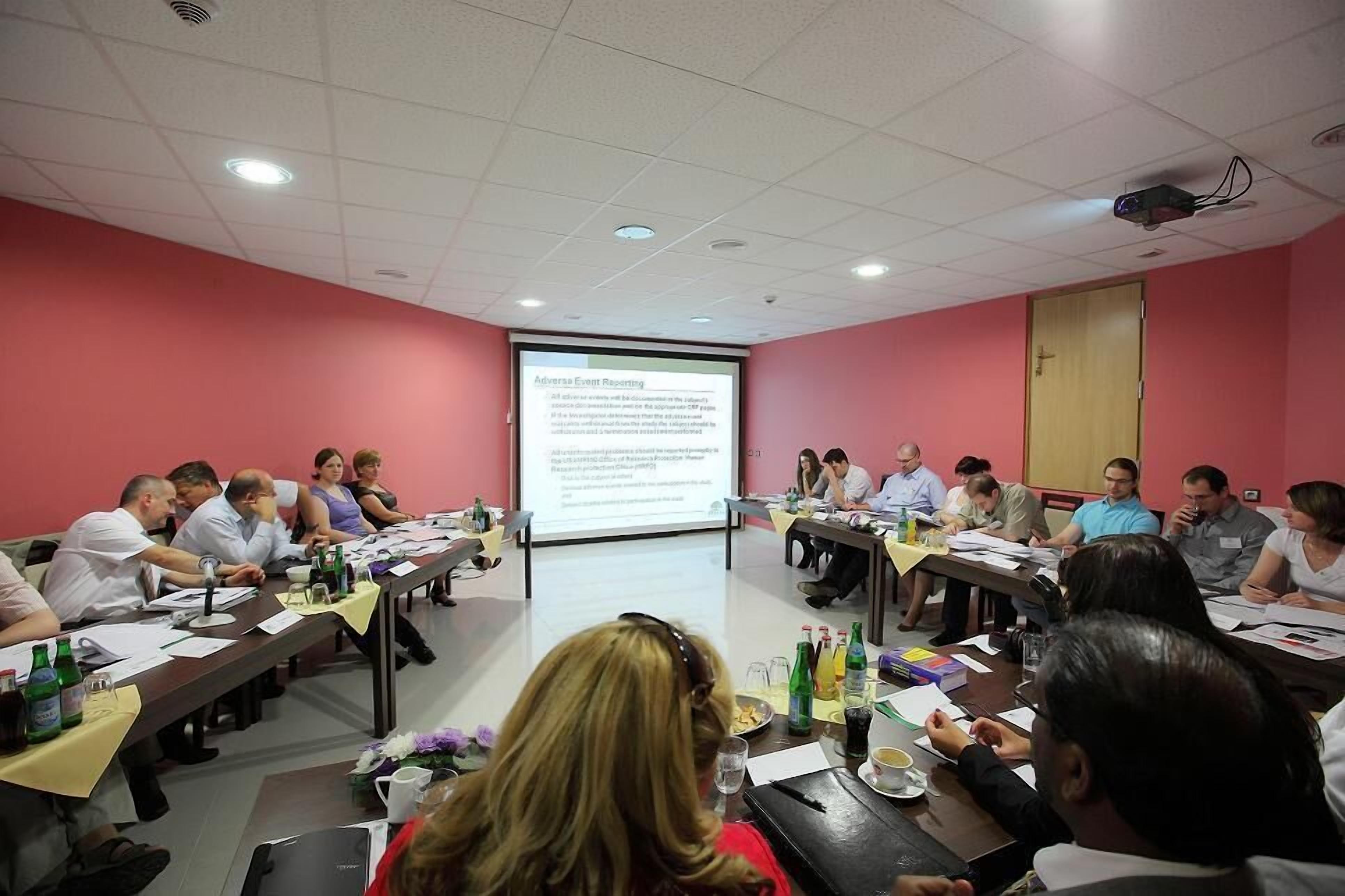 A conference room with a presentation screen, tables, and attendees.