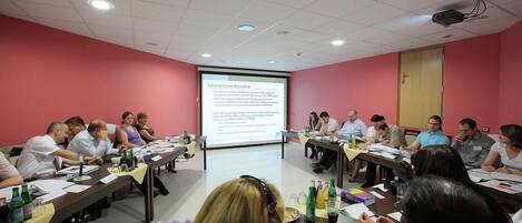 A conference room with a presentation screen, tables, and attendees.