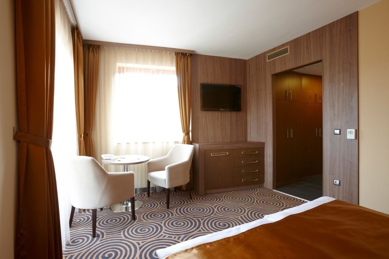 Ein Hotelzimmer mit Bett, Schreibtisch mit zwei Stühlen, einem an der Wand montierten Fernseher und einem Kleiderschrank.