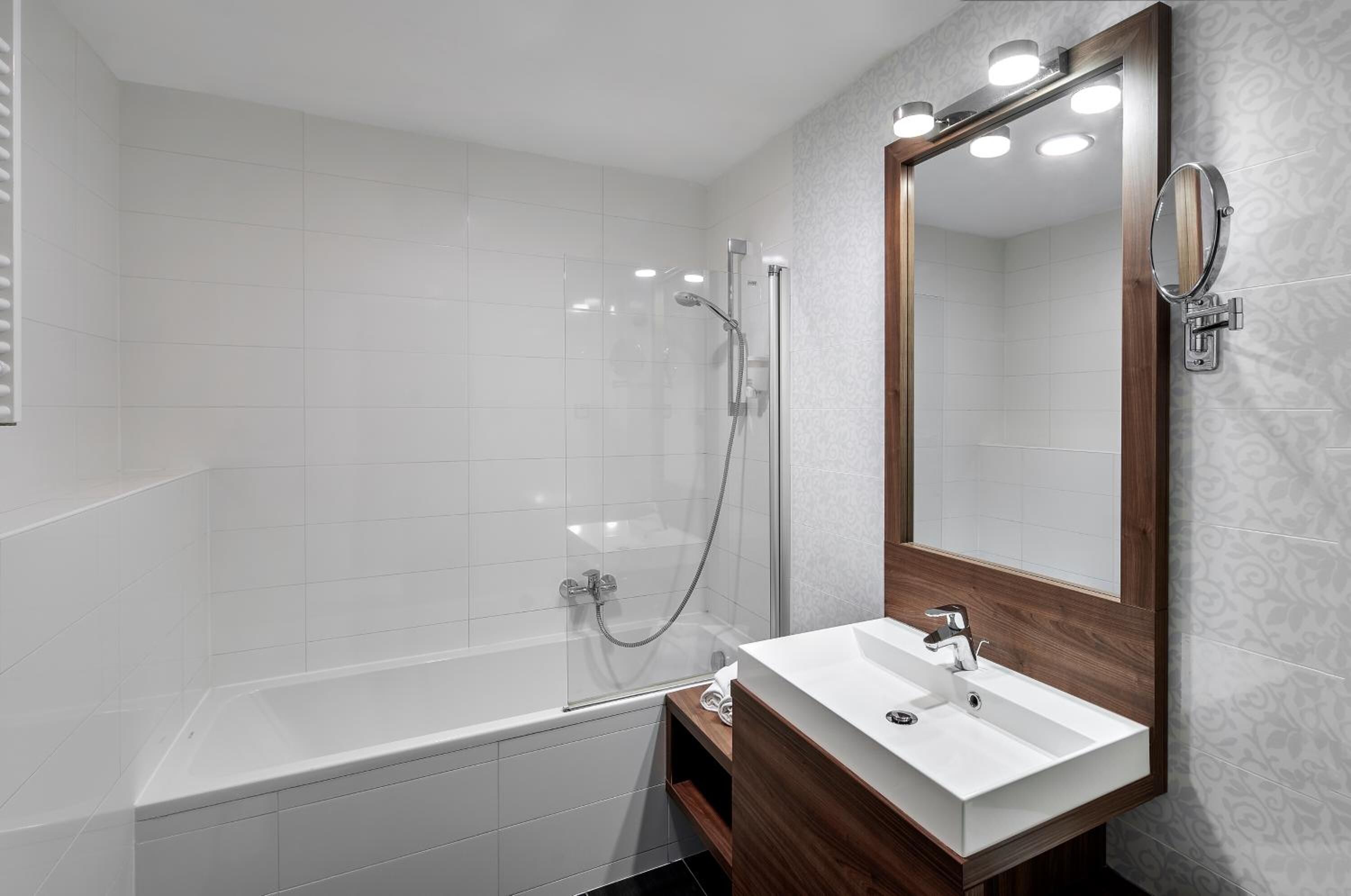 Un bagno moderno con una vasca da bagno bianca, un mobile bagno in legno con un lavabo e uno specchio grande.