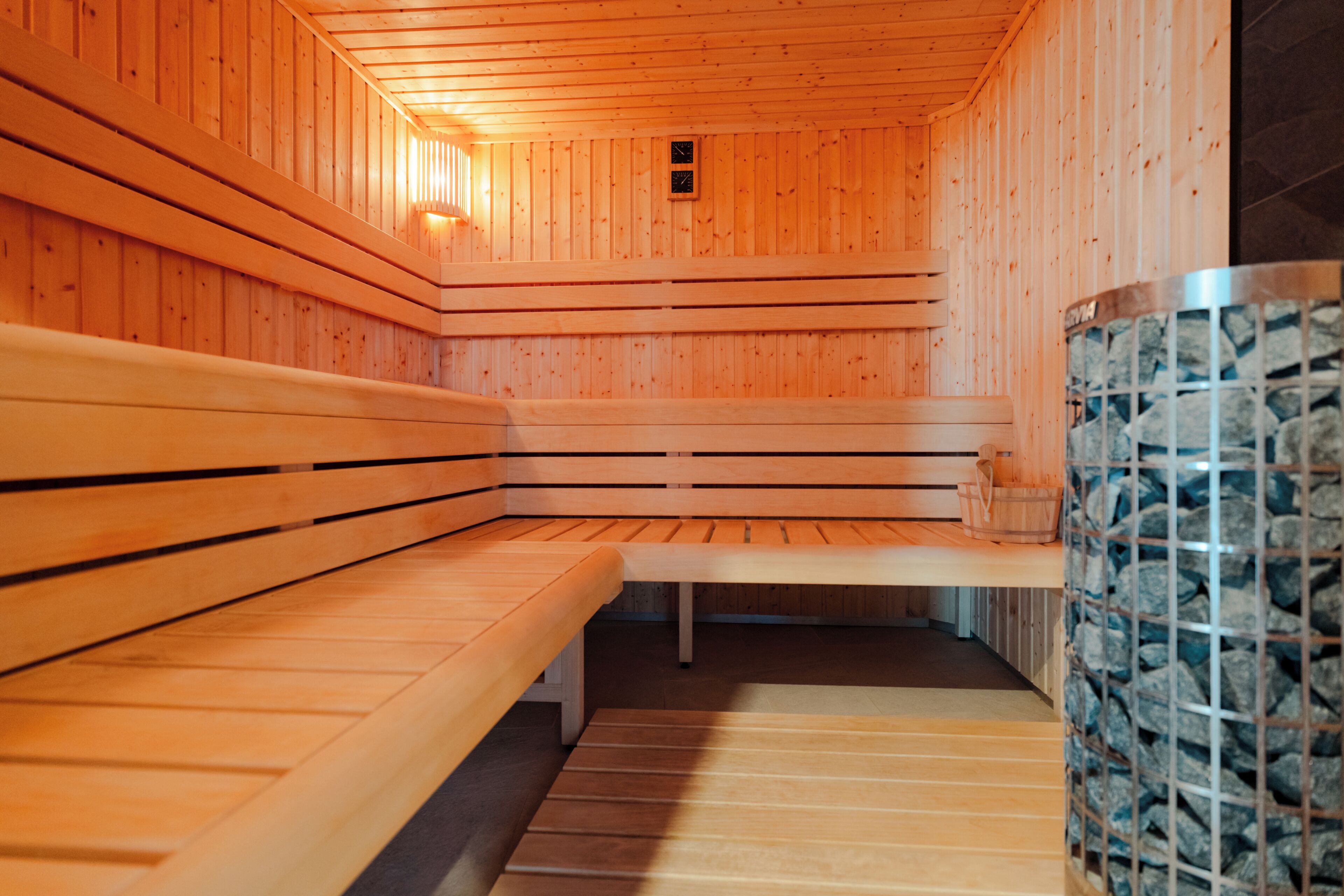 A sauna with wooden benches, a stone wall, and a small clock on the wall.