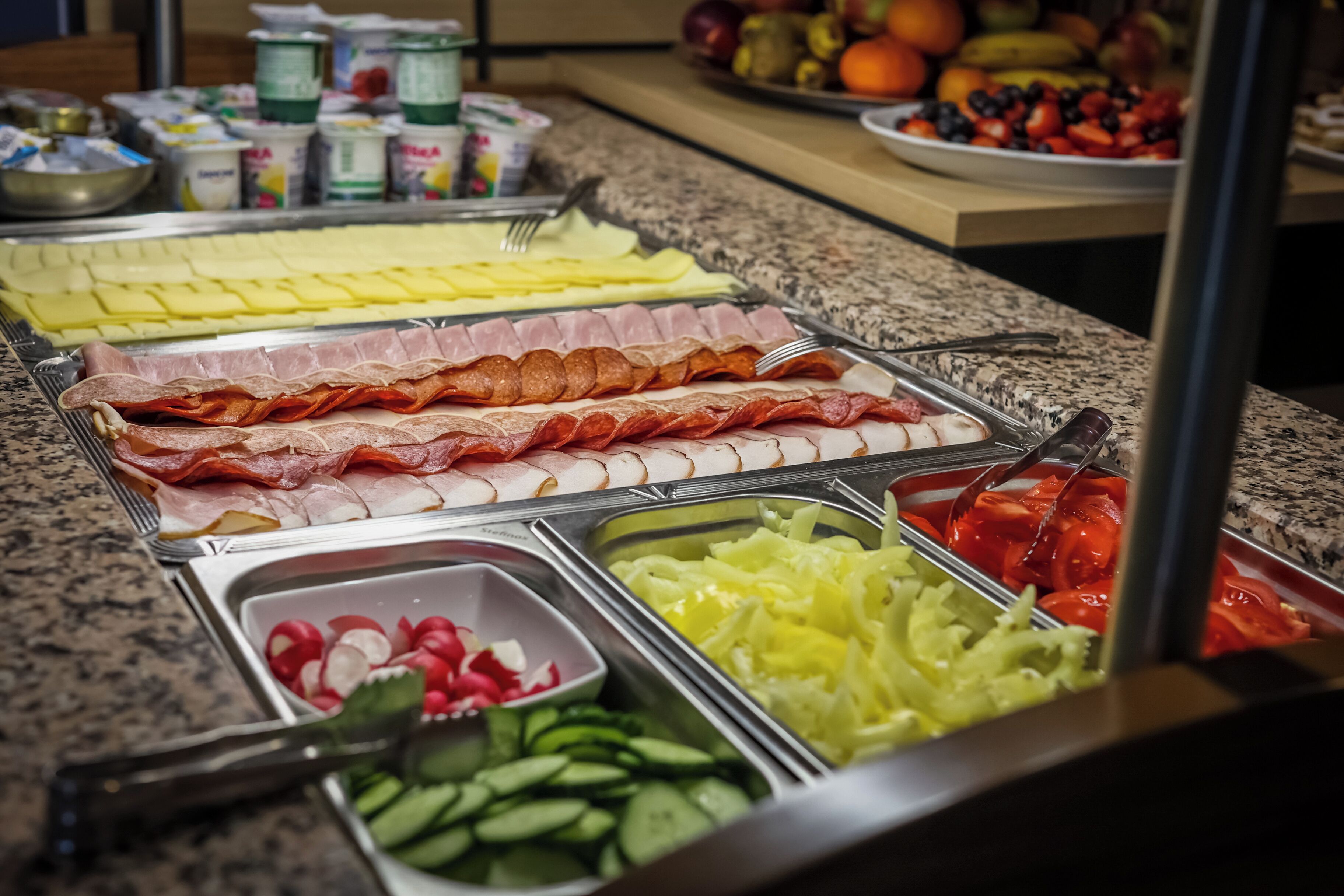 A buffet with various food options including meats, cheeses, and fresh vegetables.