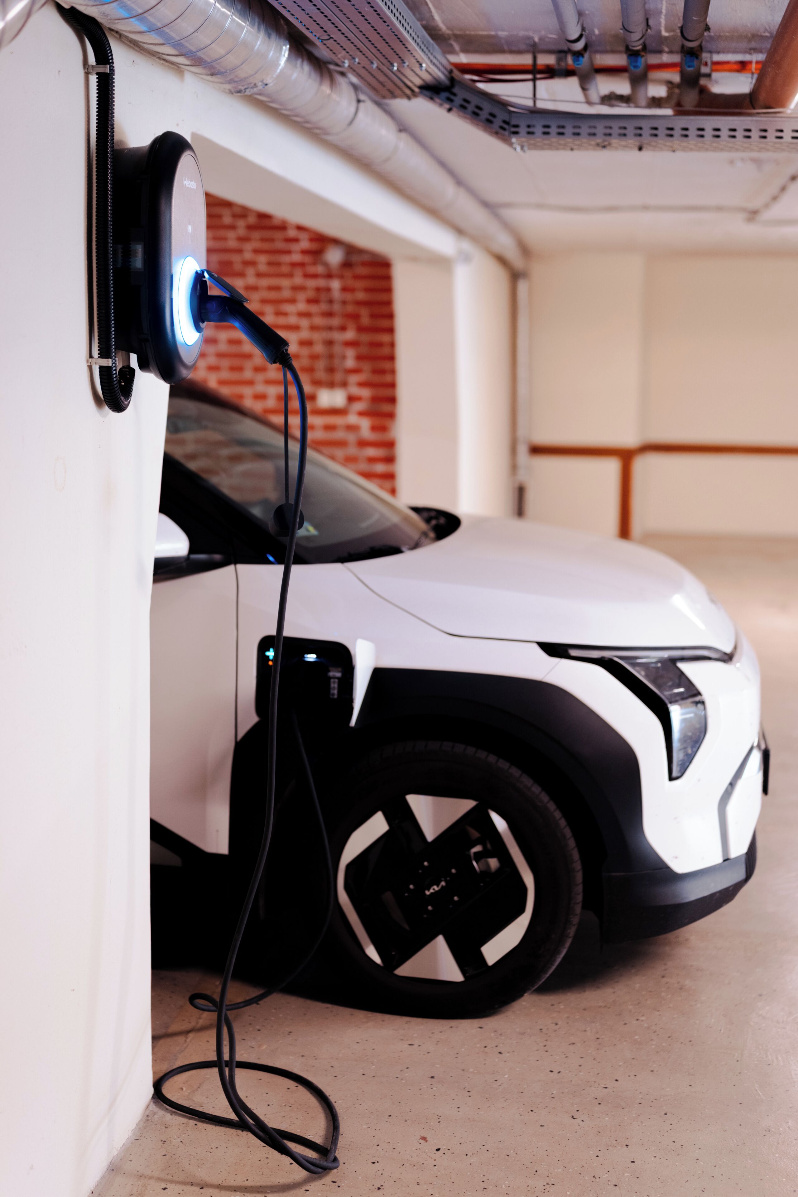 A white electric vehicle charging at a station with a visible cable and a blue light indicator.