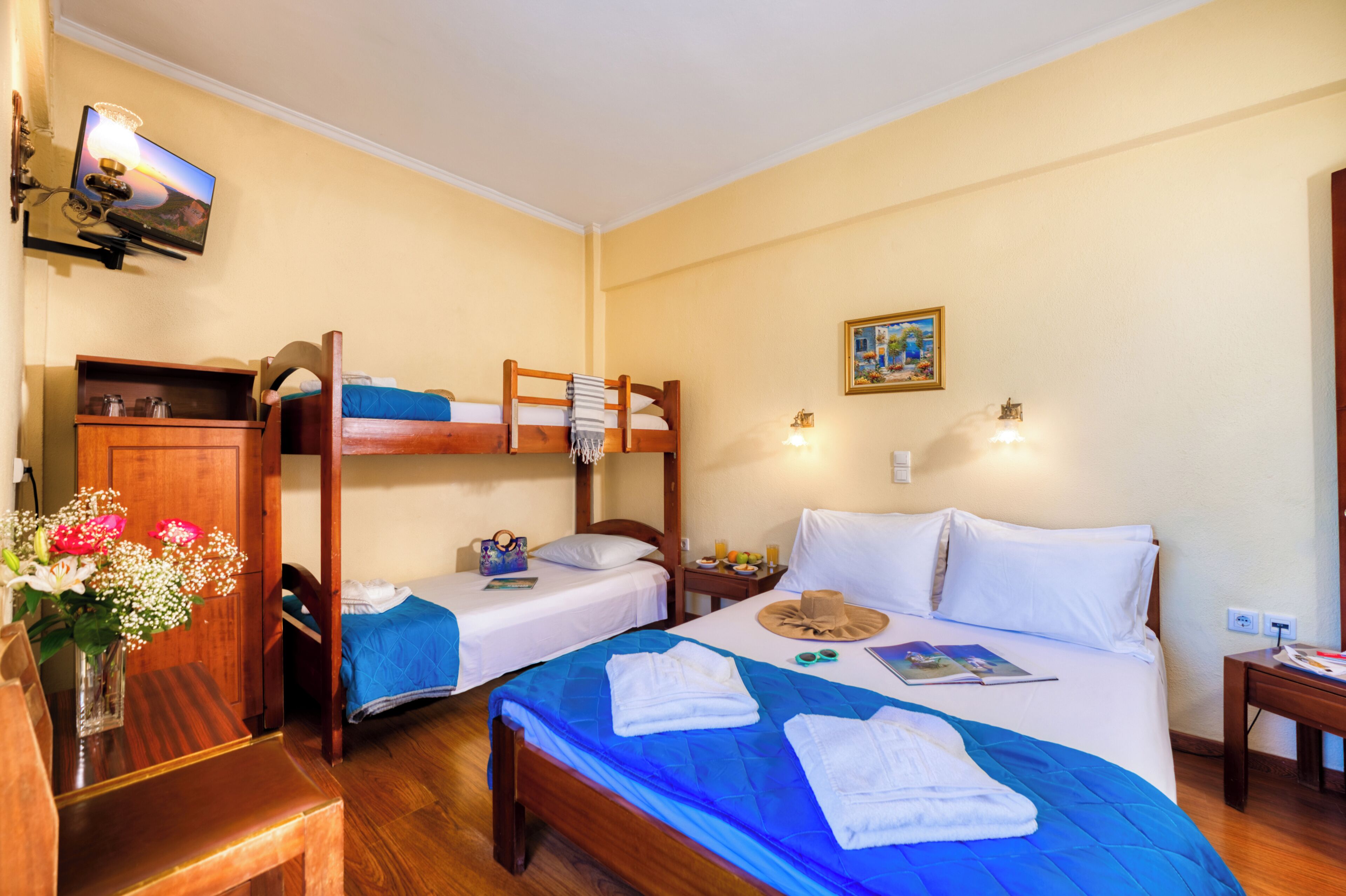 Een hotelkamer met stapelbedden, een houten bureau, een televisie en een schilderij aan de muur.