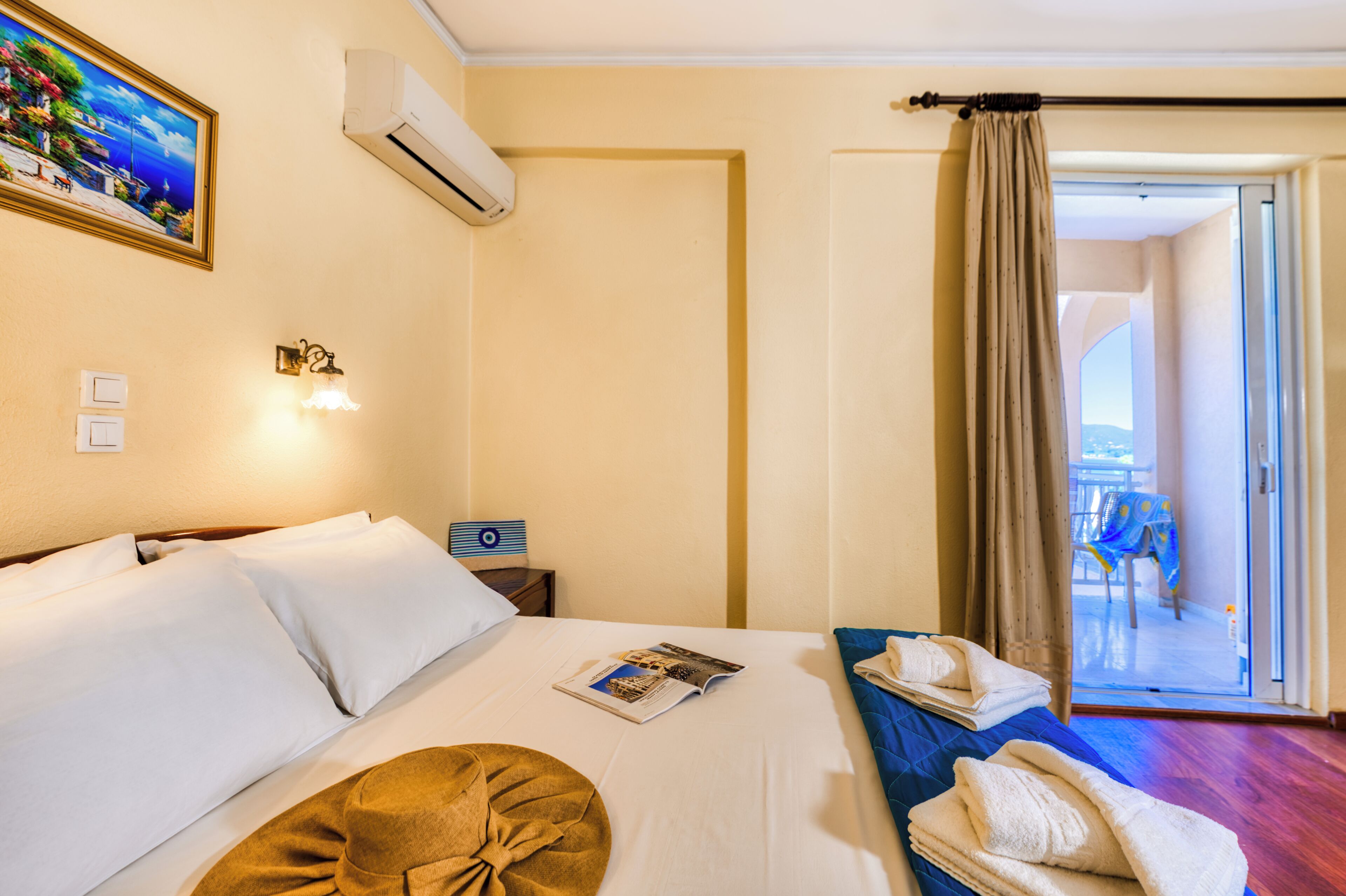 A hotel room with a bed, a nightstand, a reading lamp, a painting, an air conditioning unit, and a view of the balcony.